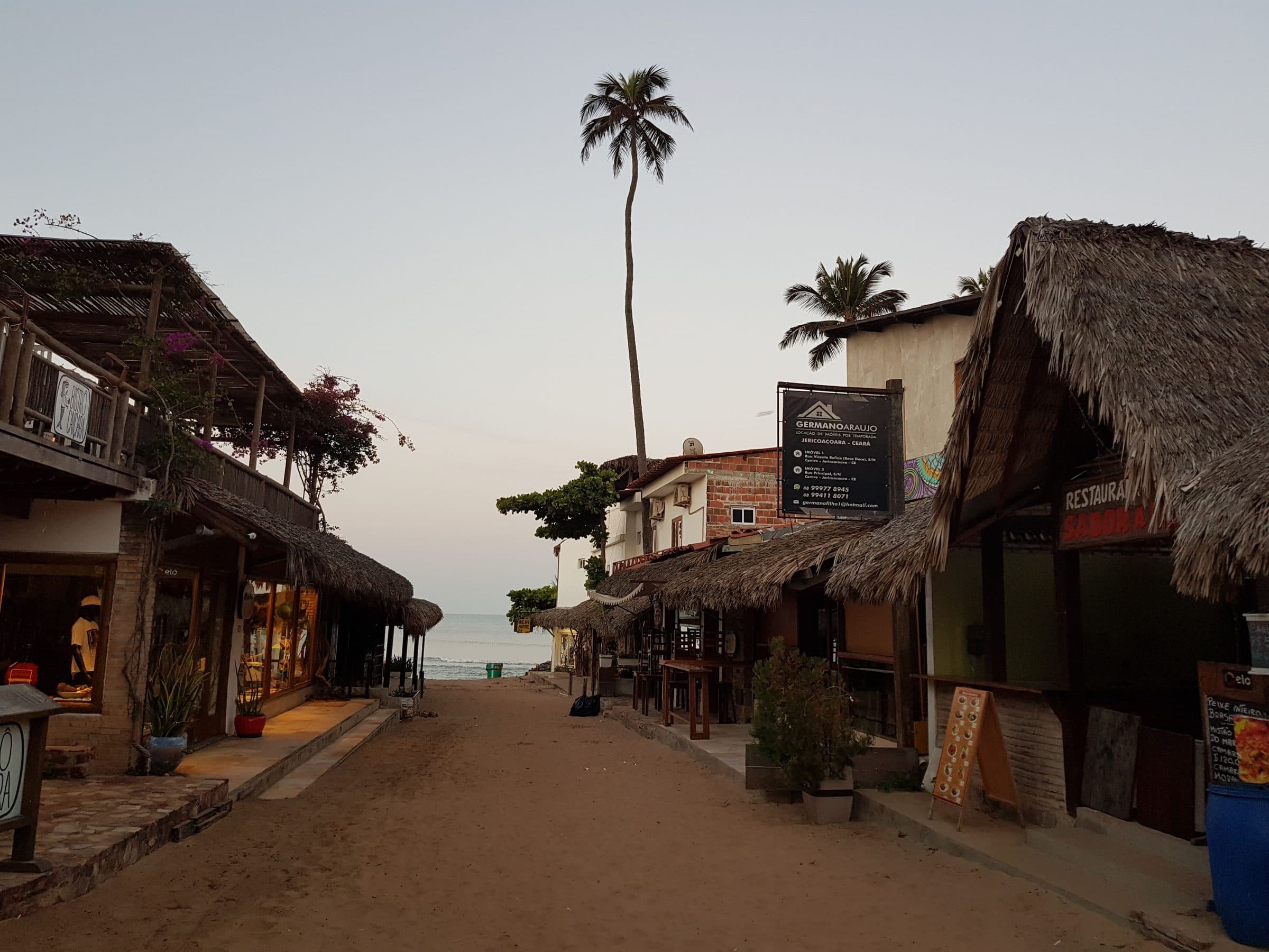 Rua em Jericoacoara ao entardecer com lojas entre palmeiras e telhados de palha