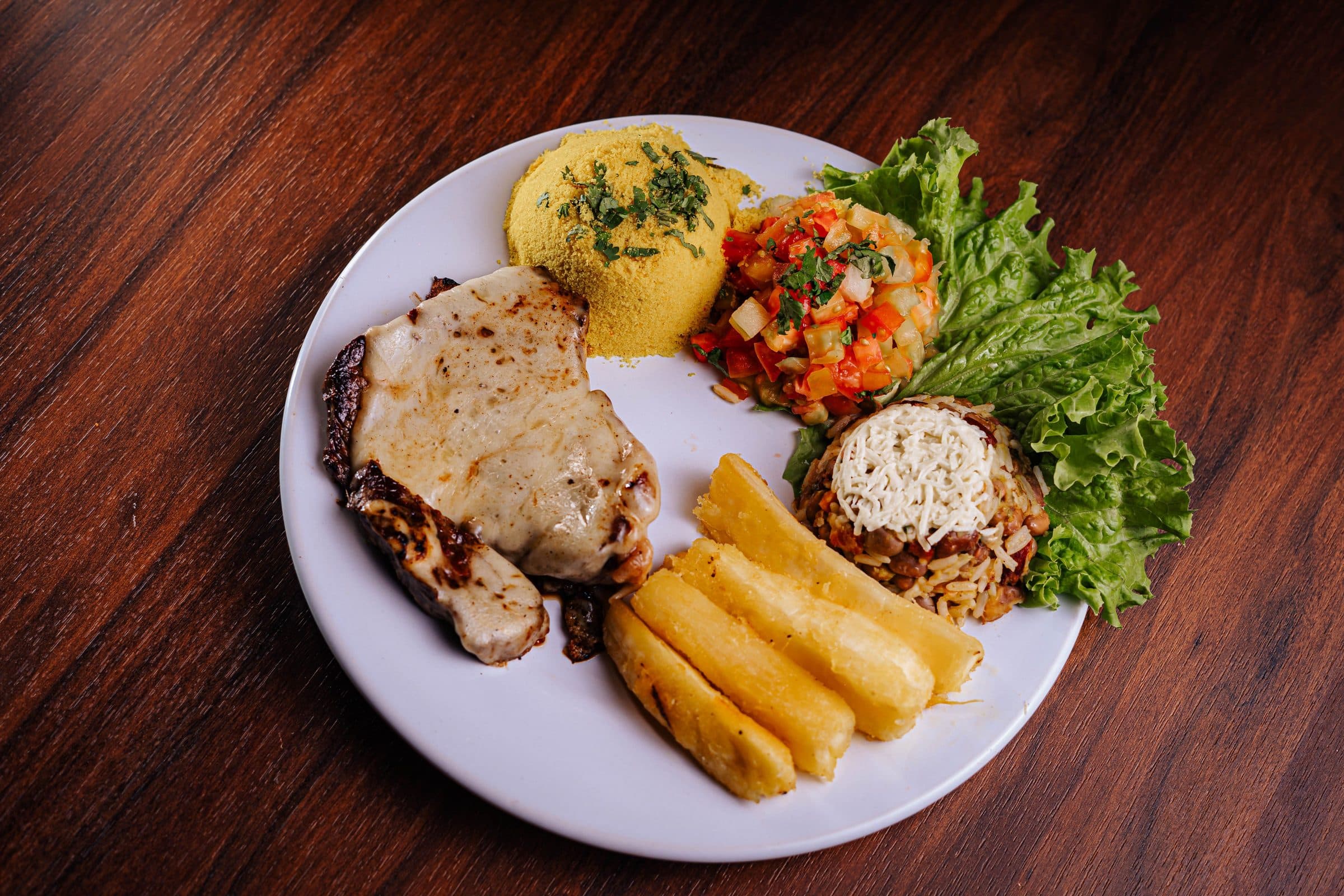 Prato de comida brasileira com bisteca de porco, arroz, feijão e salada fresca