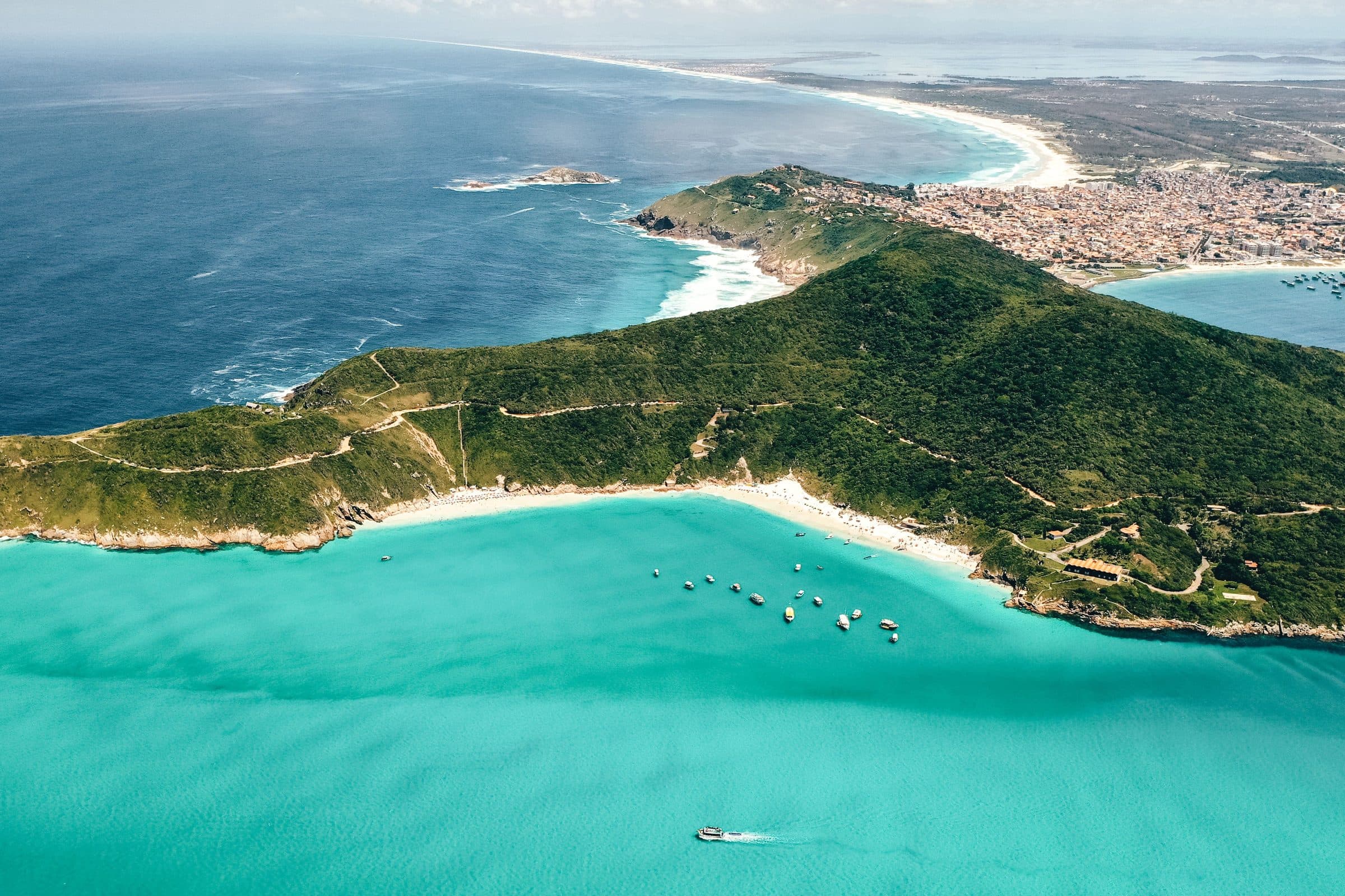 Vista aérea de mar azul-turquesa com uma ilha de vegetação densa e cidade litorânea ao fundo