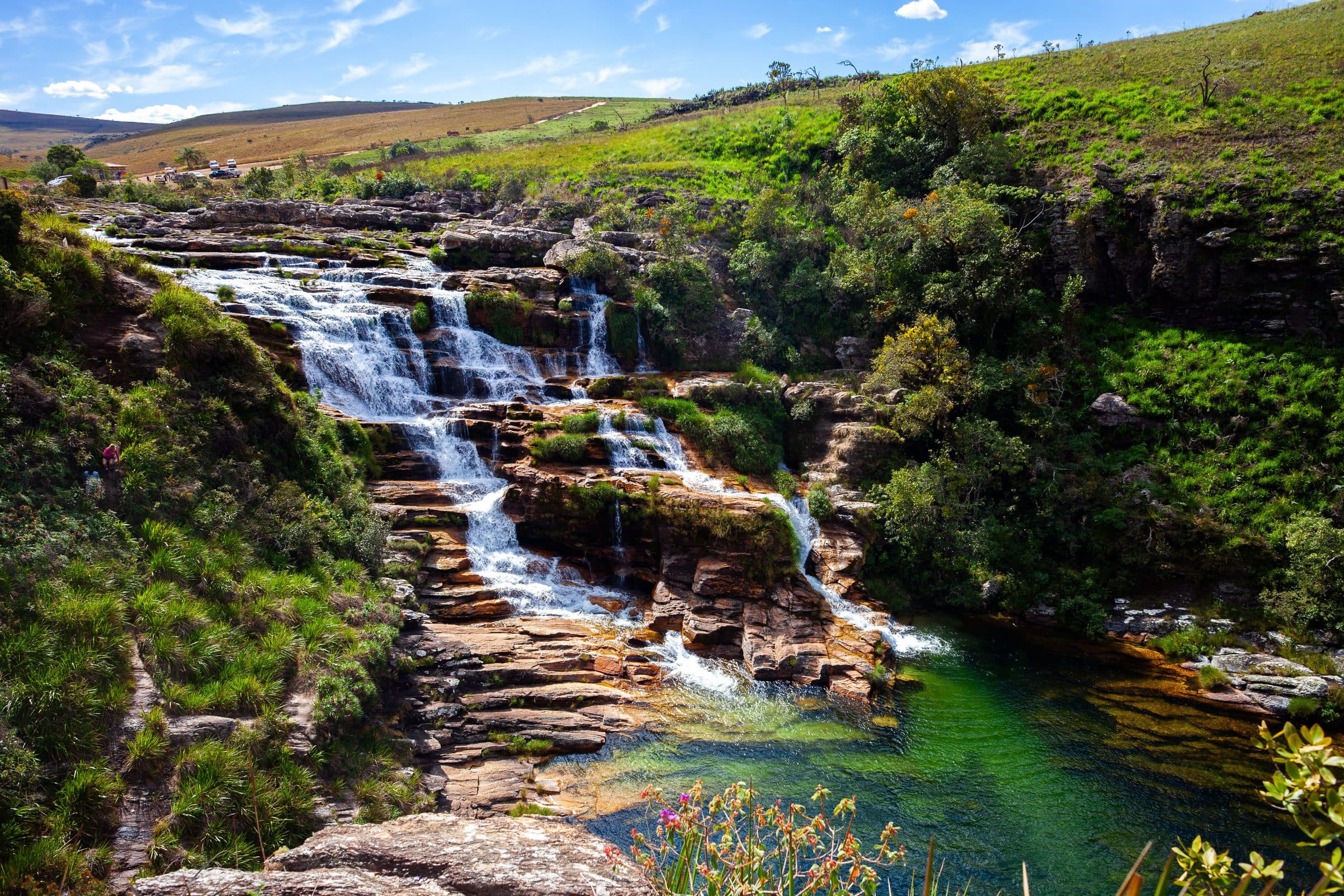 Cachoeira desaguando em uma piscina natural de águas claras, cercada por vegetação densa
