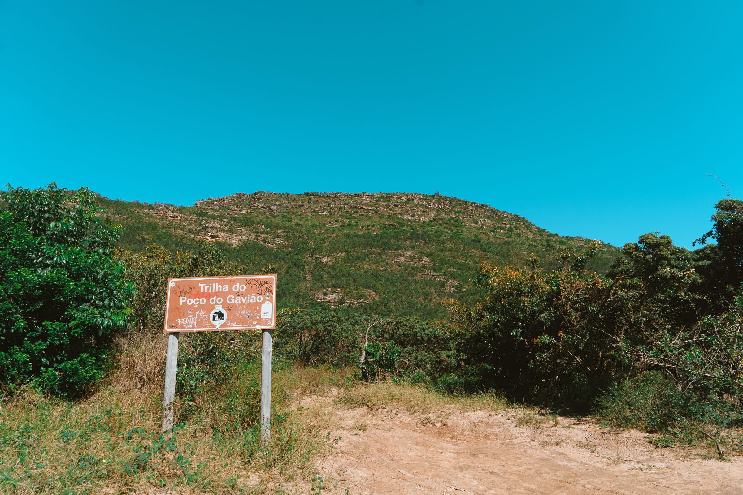 Trilha de caminhada cercada por vegetação no Poço do Gavião sob céu azul