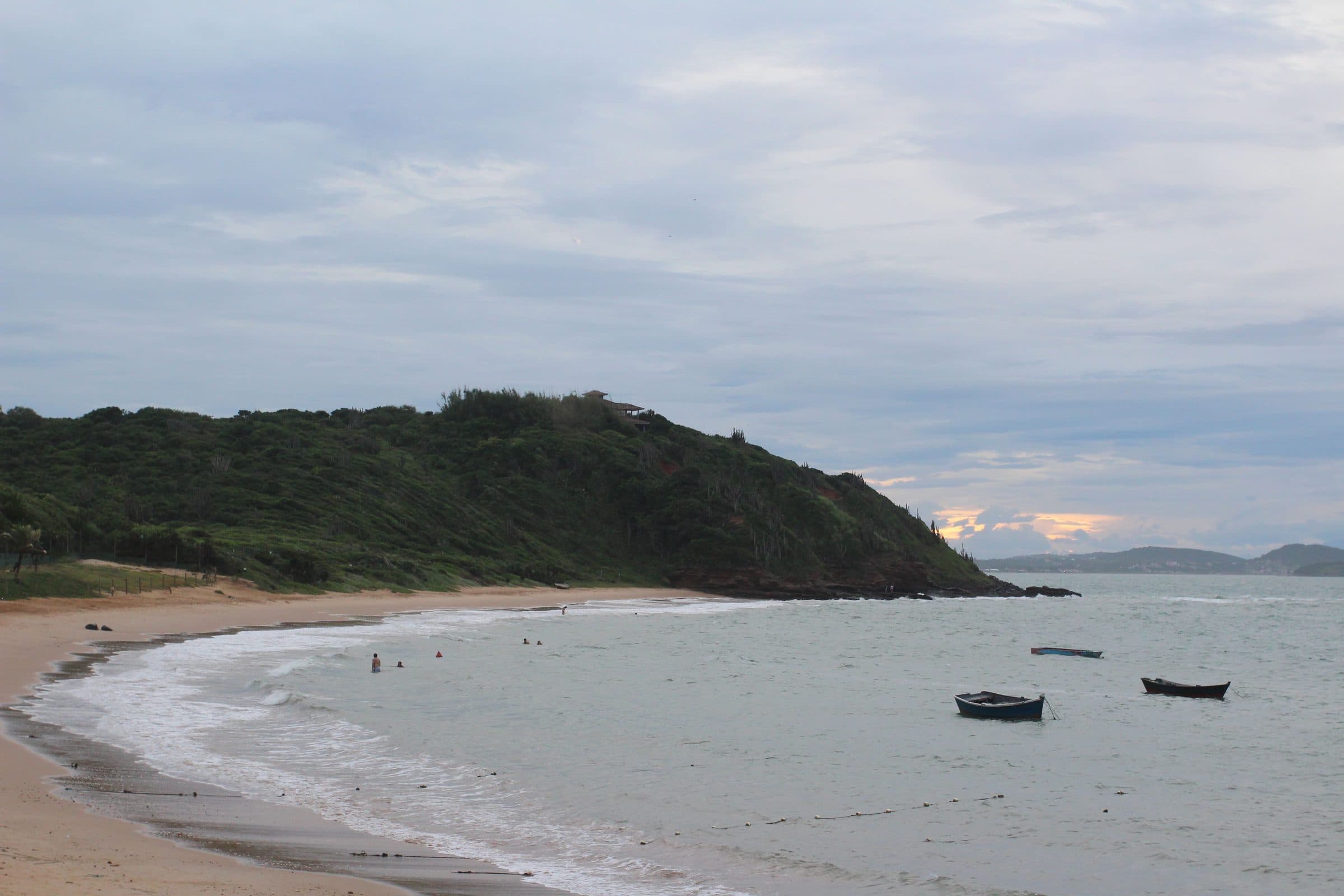 Praia em Armação dos Búzios com barcos de pesca e vegetação ao fundo
