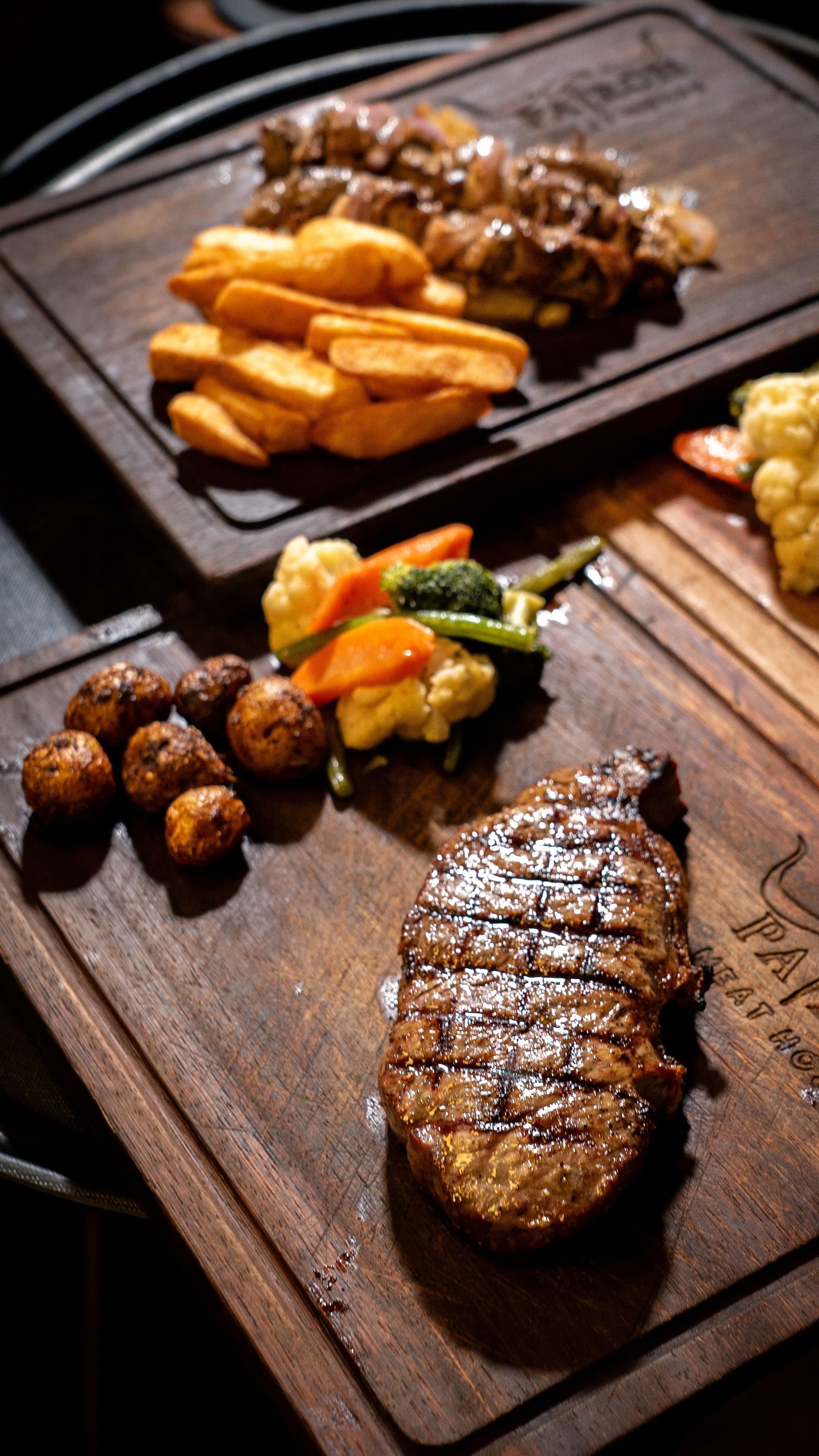 Bife grelhado com legumes coloridos e batatas servido em uma tábua de madeira