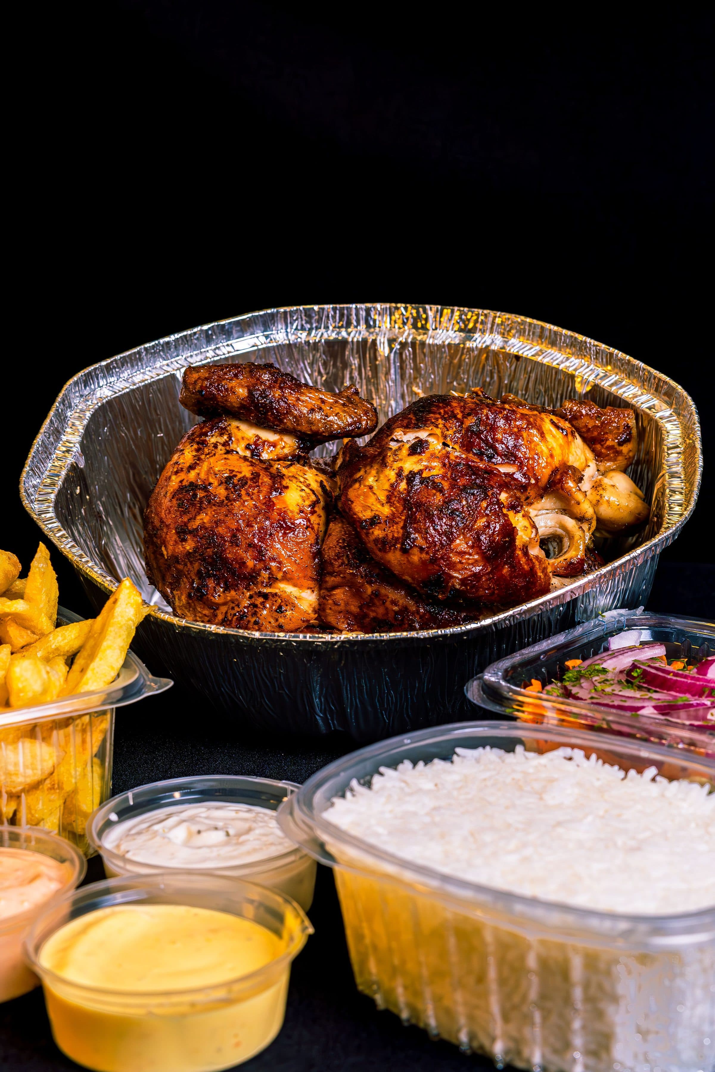 Frango assado servido com batatas fritas, arroz e molhos