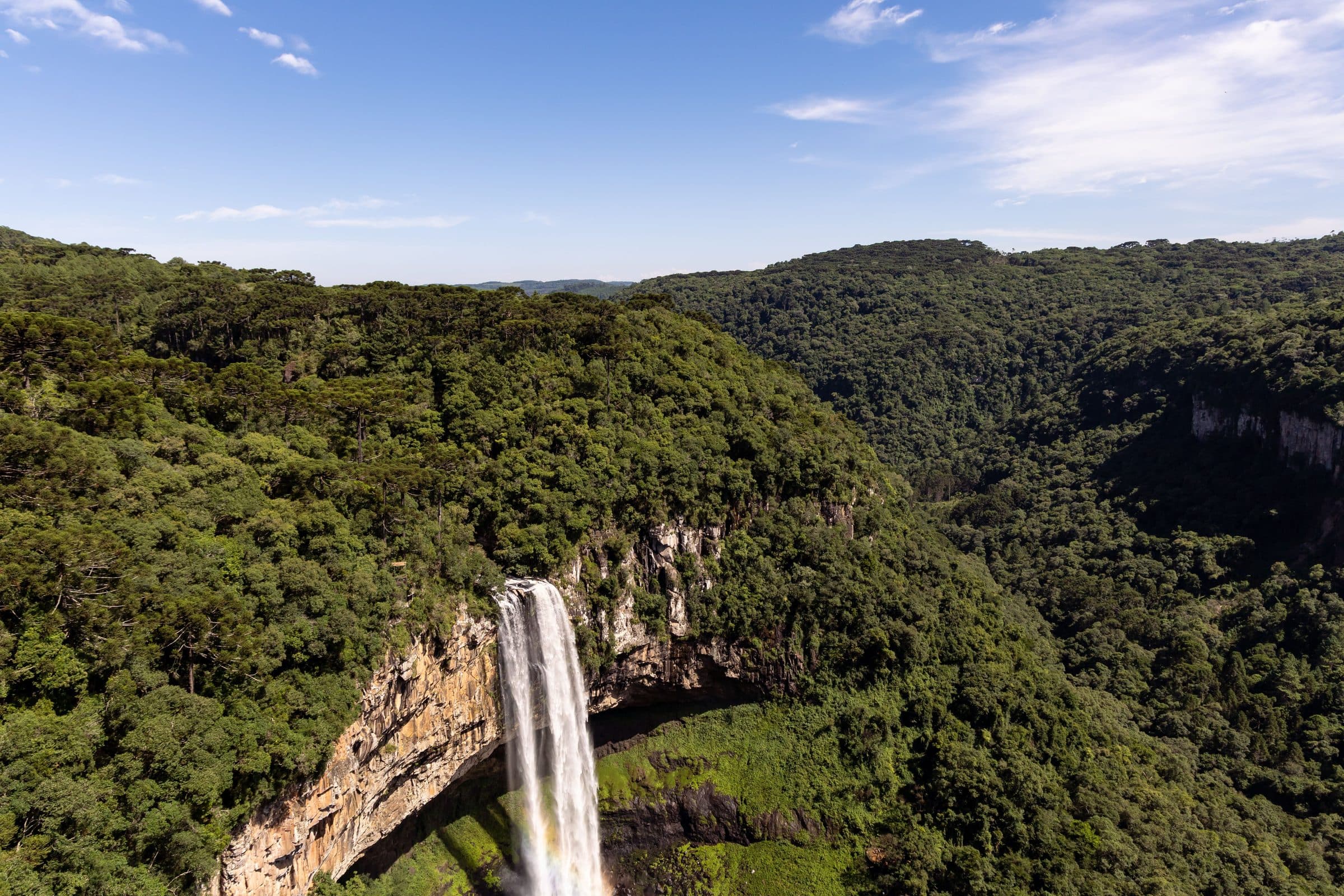 Vista aérea da Cascata do Caracol cercada por floresta verde sob céu limpo em Gramado