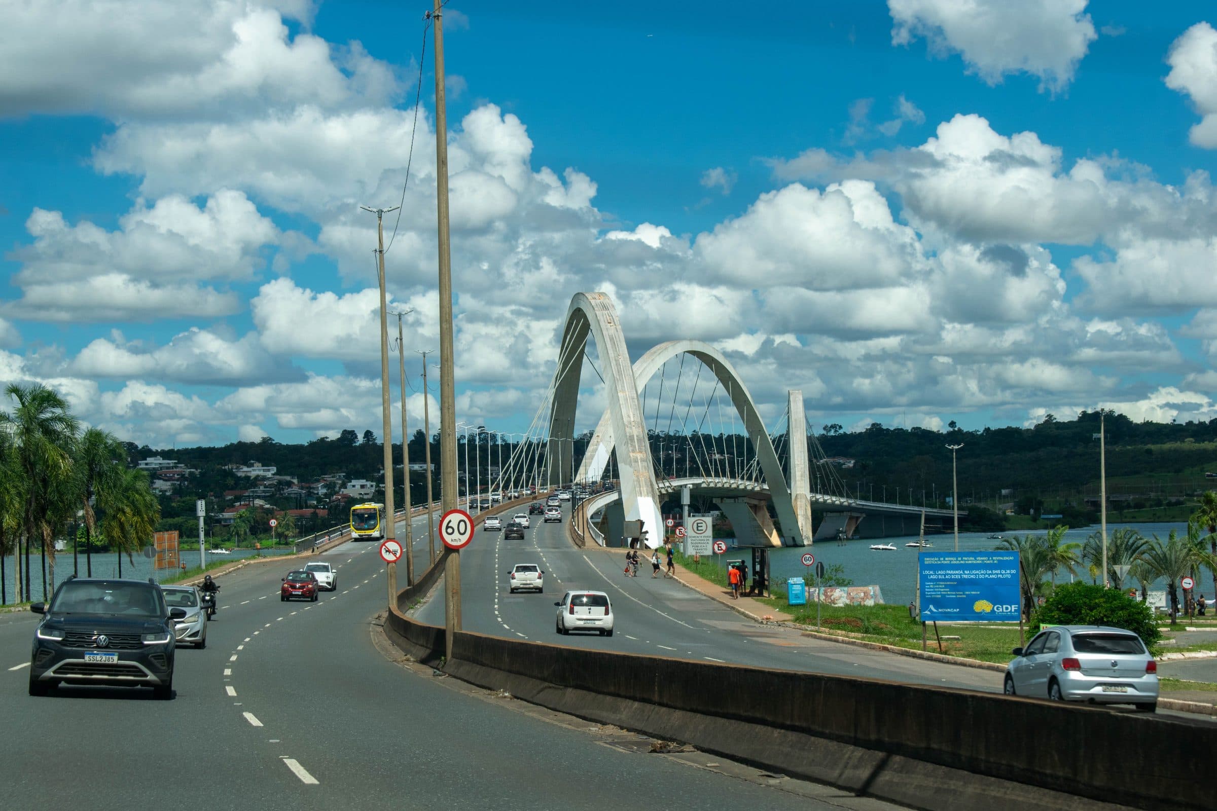Ponte JK em Brasília com trânsito de veículos, vegetação e céu azul com nuvens
