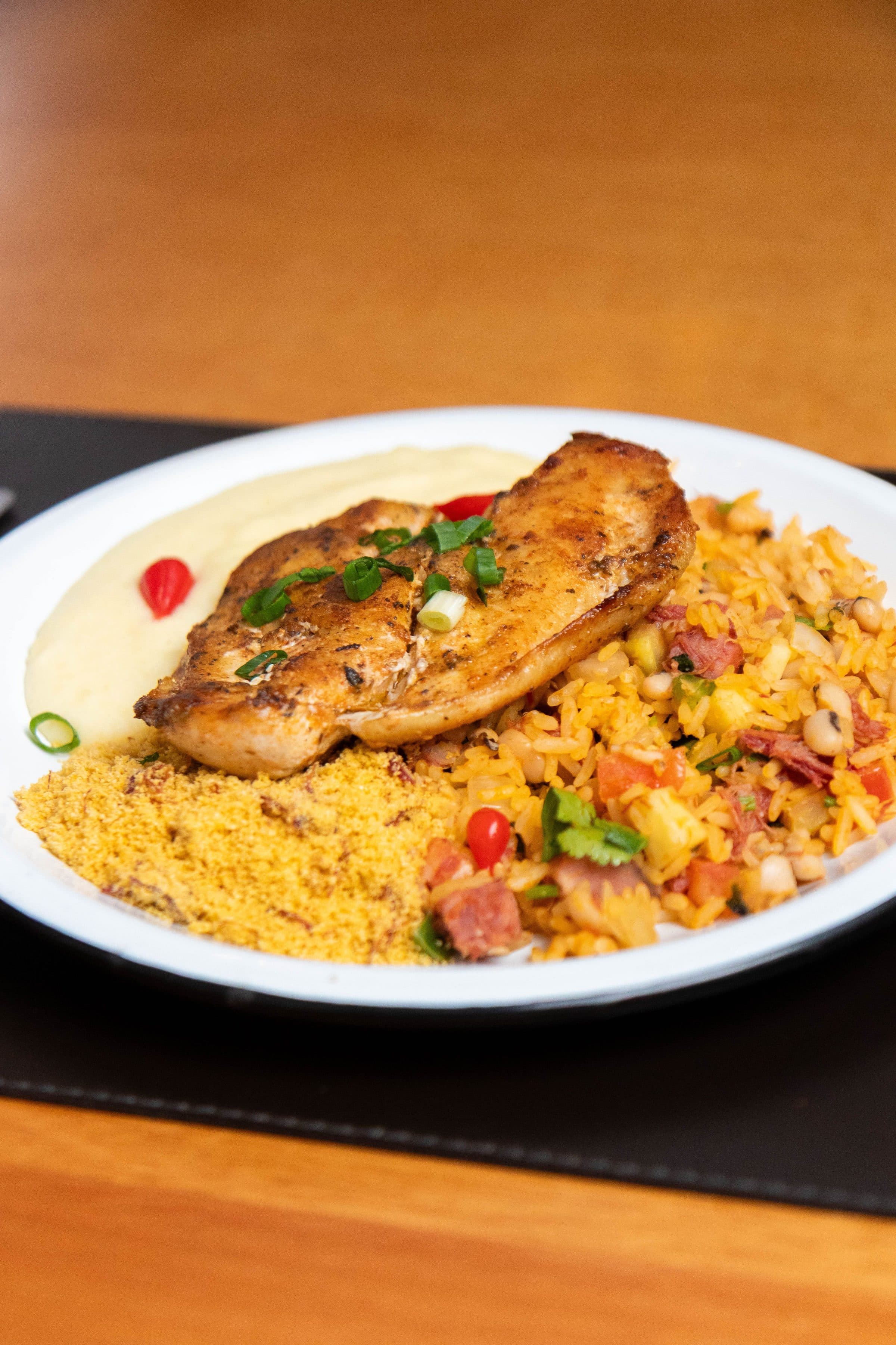 Prato branco com frango grelhado, farofa e arroz colorido