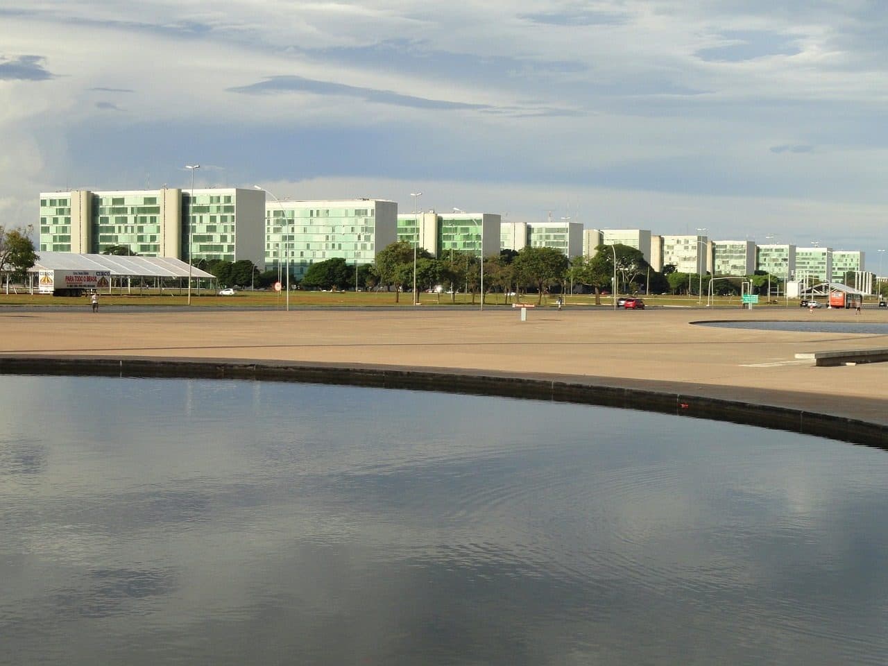 Vista de prédios e árvores à beira do lago em Brasília sob céu com nuvens