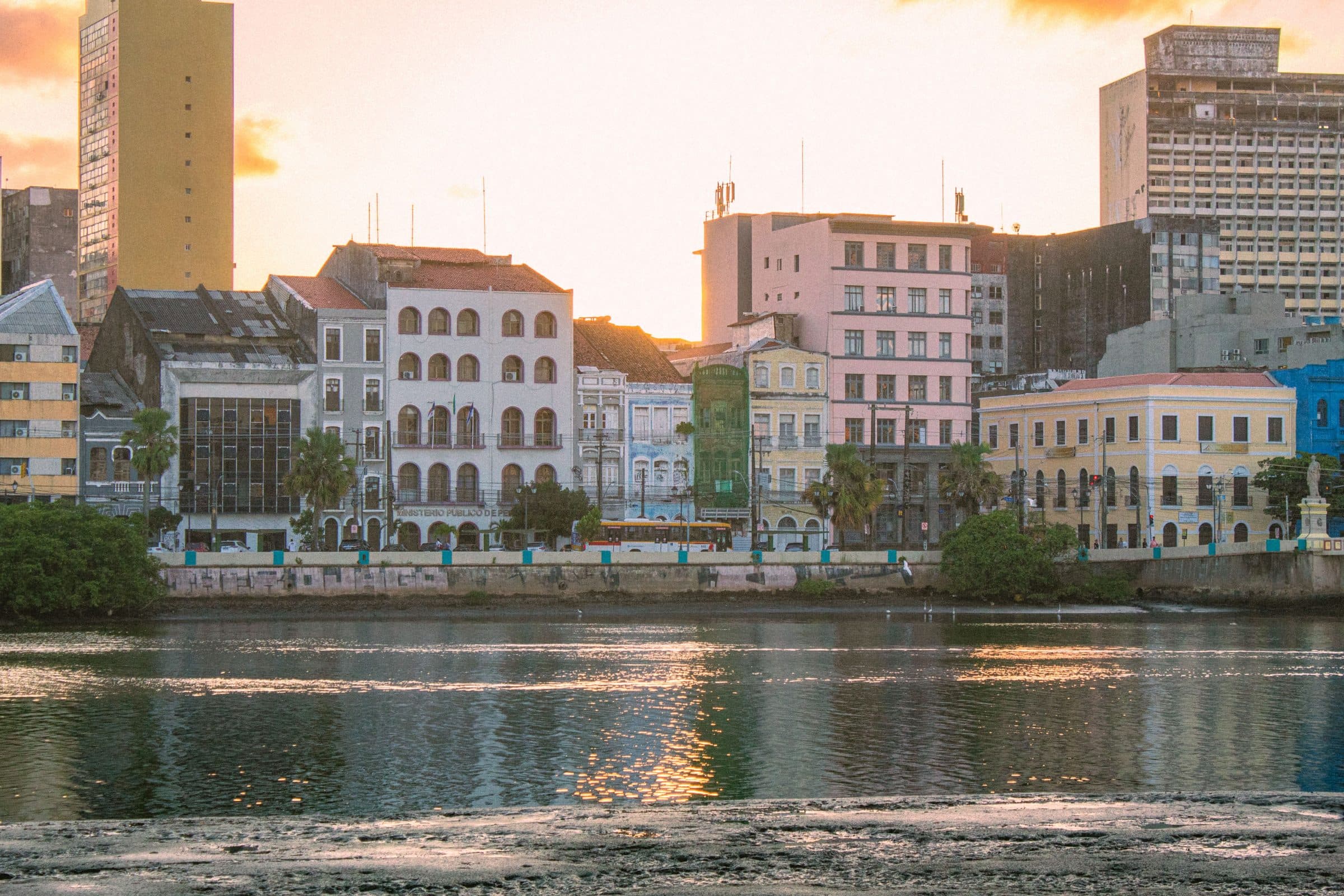 Arquitetura histórica de Recife à beira do rio refletida na água ao pôr do sol