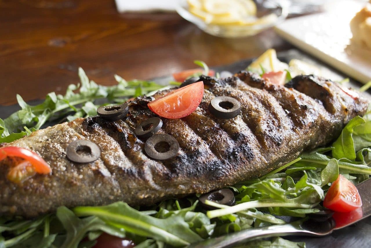 Prato com peixe assado acompanhado de rúcula, tomates e azeitonas sobre a mesa