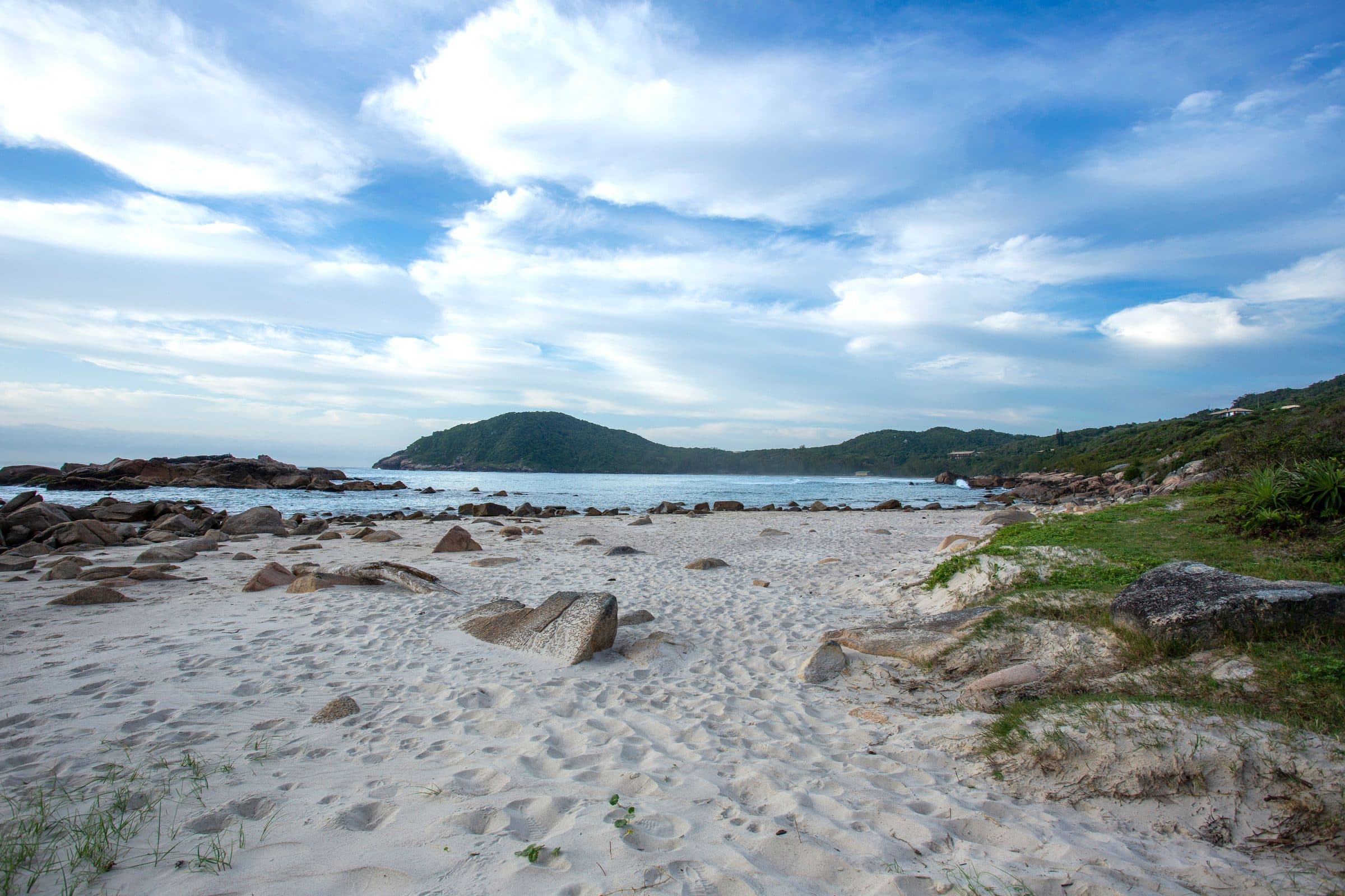 Vista da praia de Garopaba com faixa de areia, rochas e céu nublado