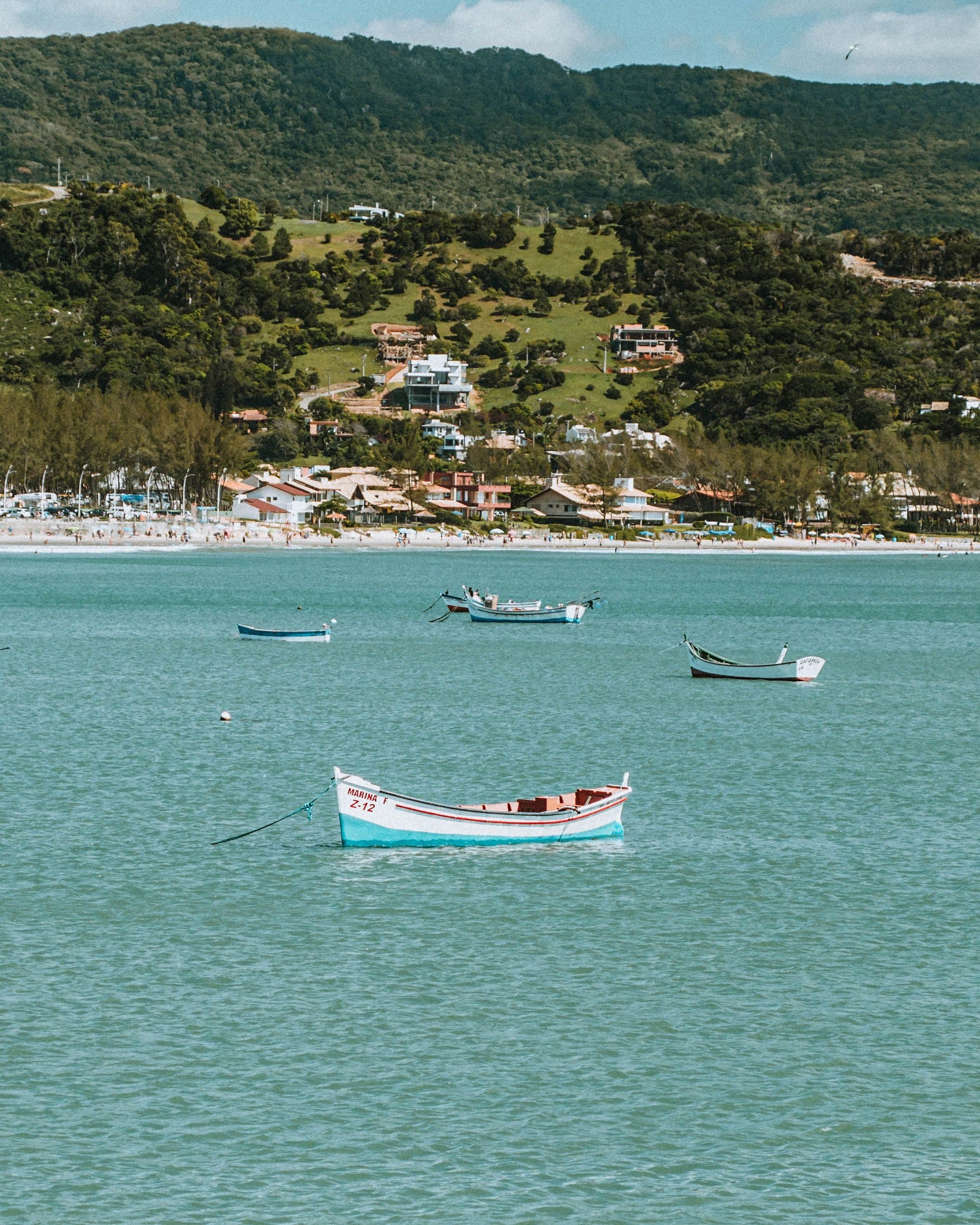 Barcos flutuando na Baía de Garopaba com morros verdes ao fundo