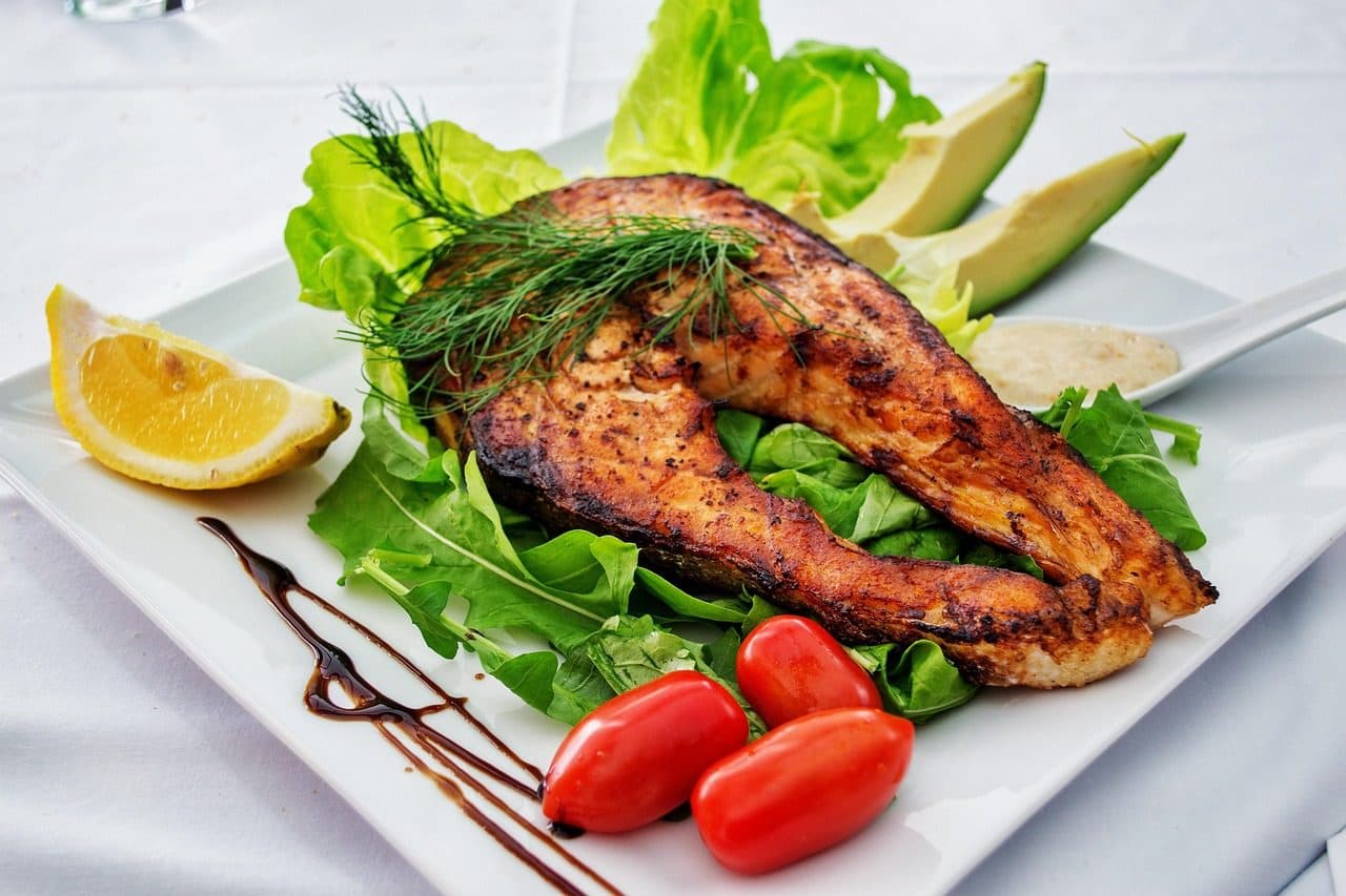 Filé de salmão grelhado servido em prato branco acompanhado de salada com alface, tomate e abacate