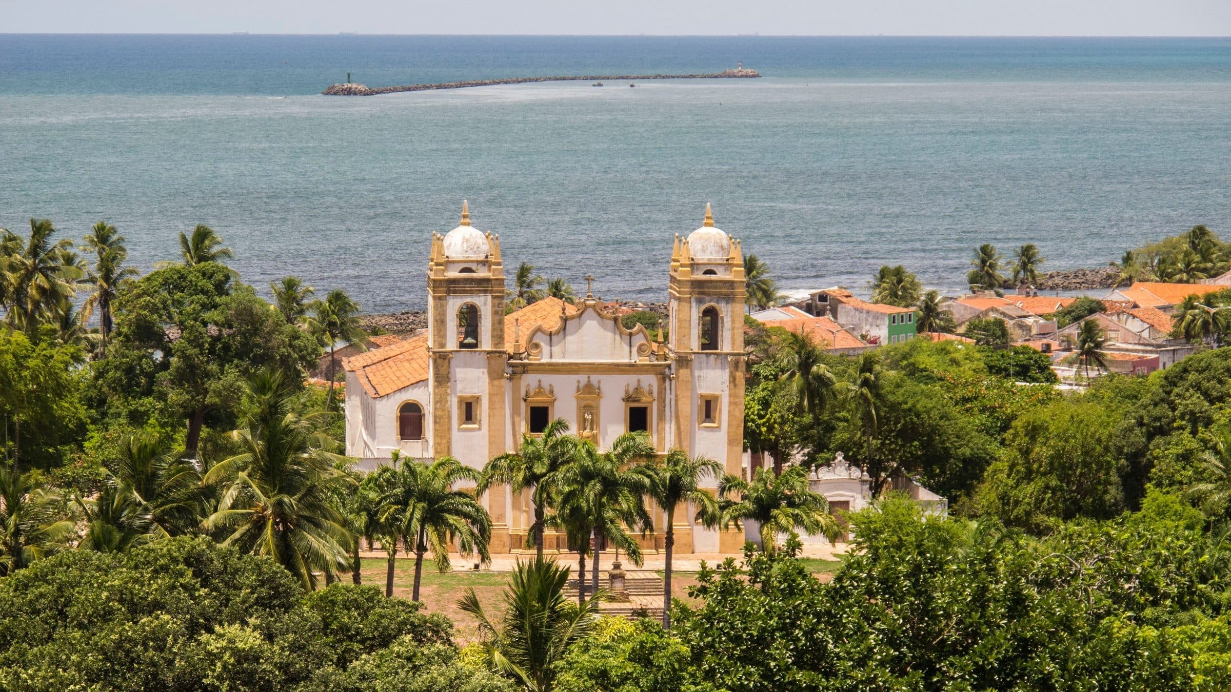 Igreja histórica cercada por vegetação em Olinda com o mar ao fundo