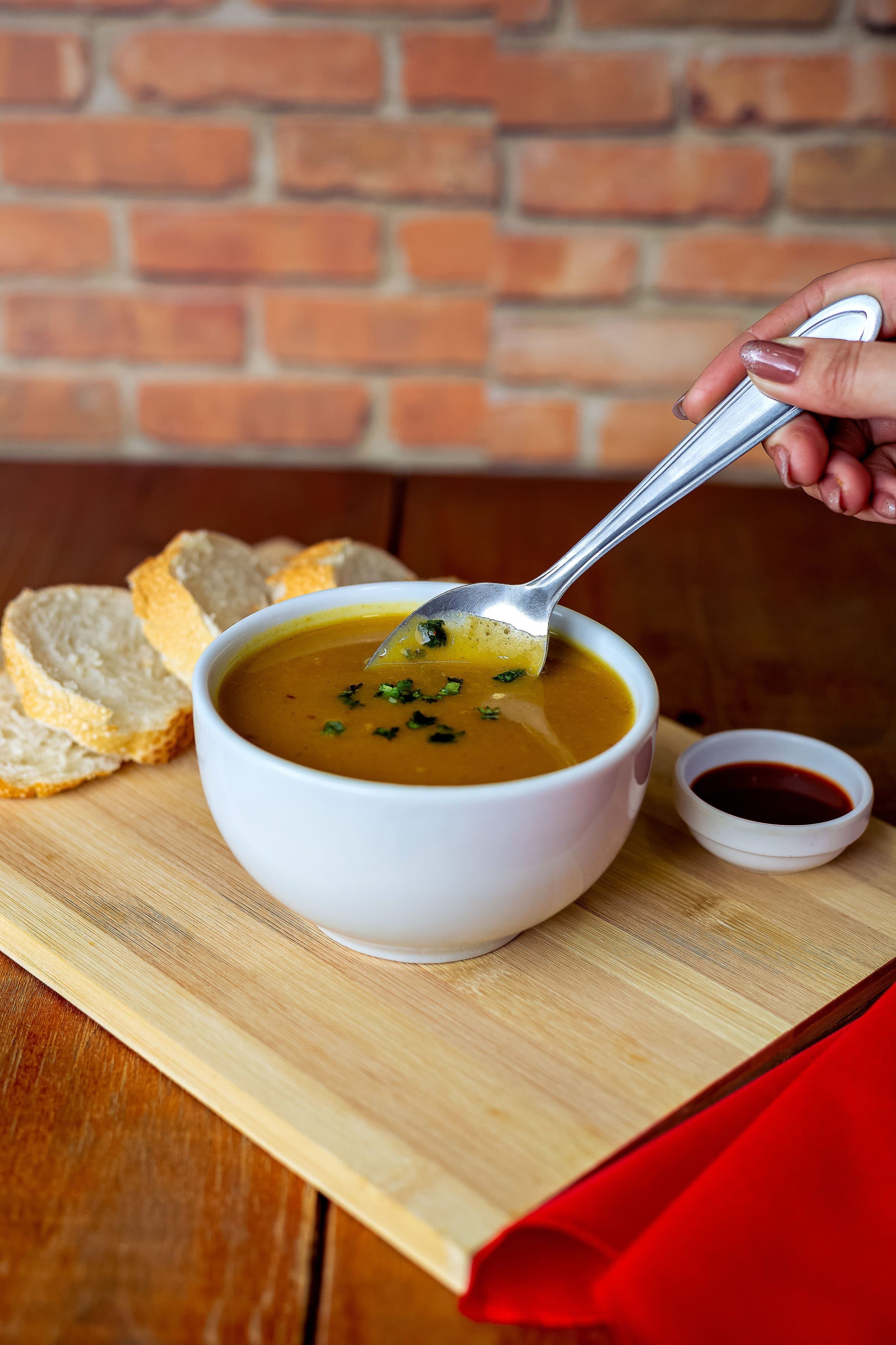 Tigela de sopa de abóbora servida com fatias de pão sobre tábua de madeira