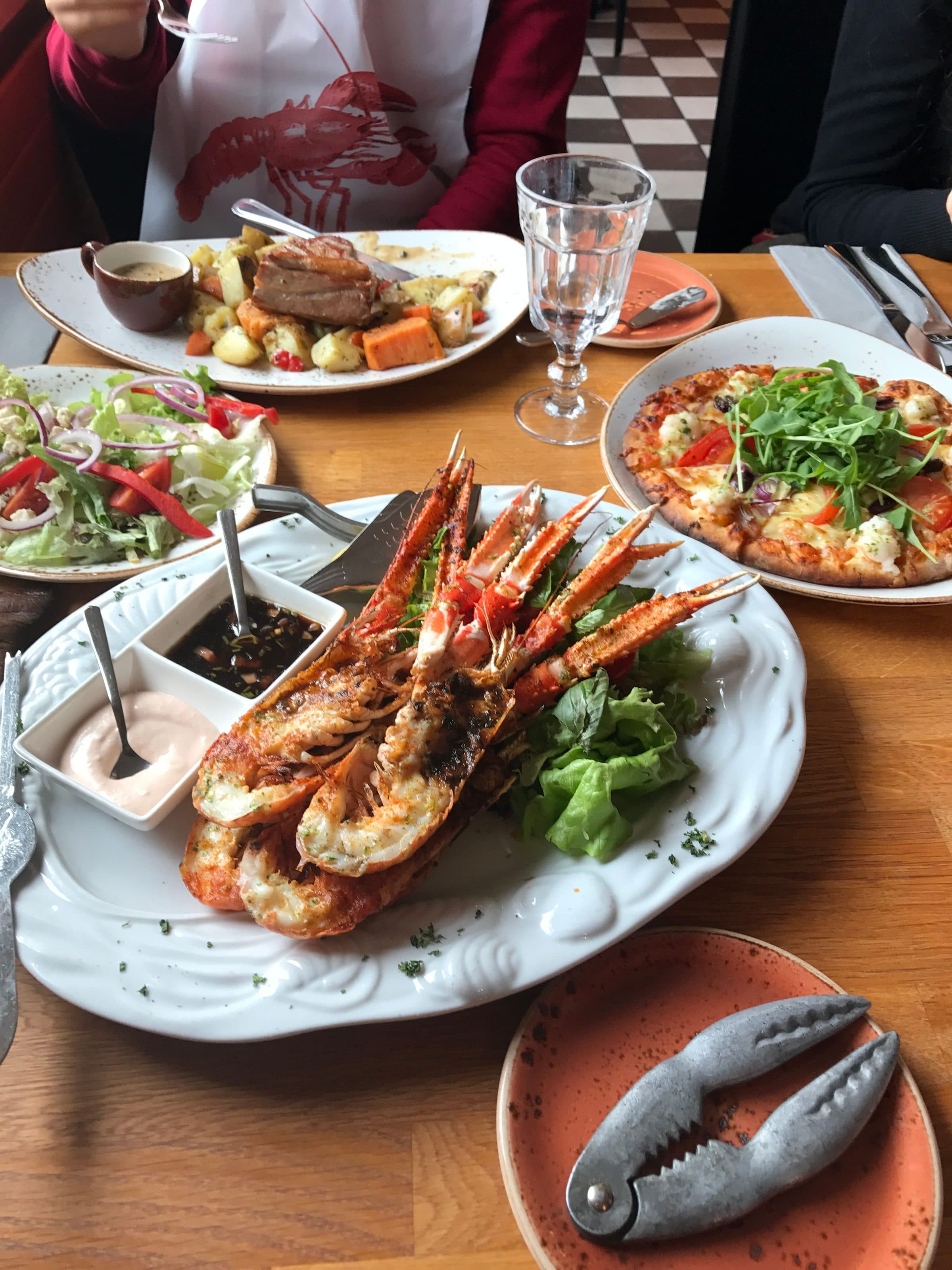 Mesa de restaurante com pratos de lagosta, frutos do mar, pizza e salada