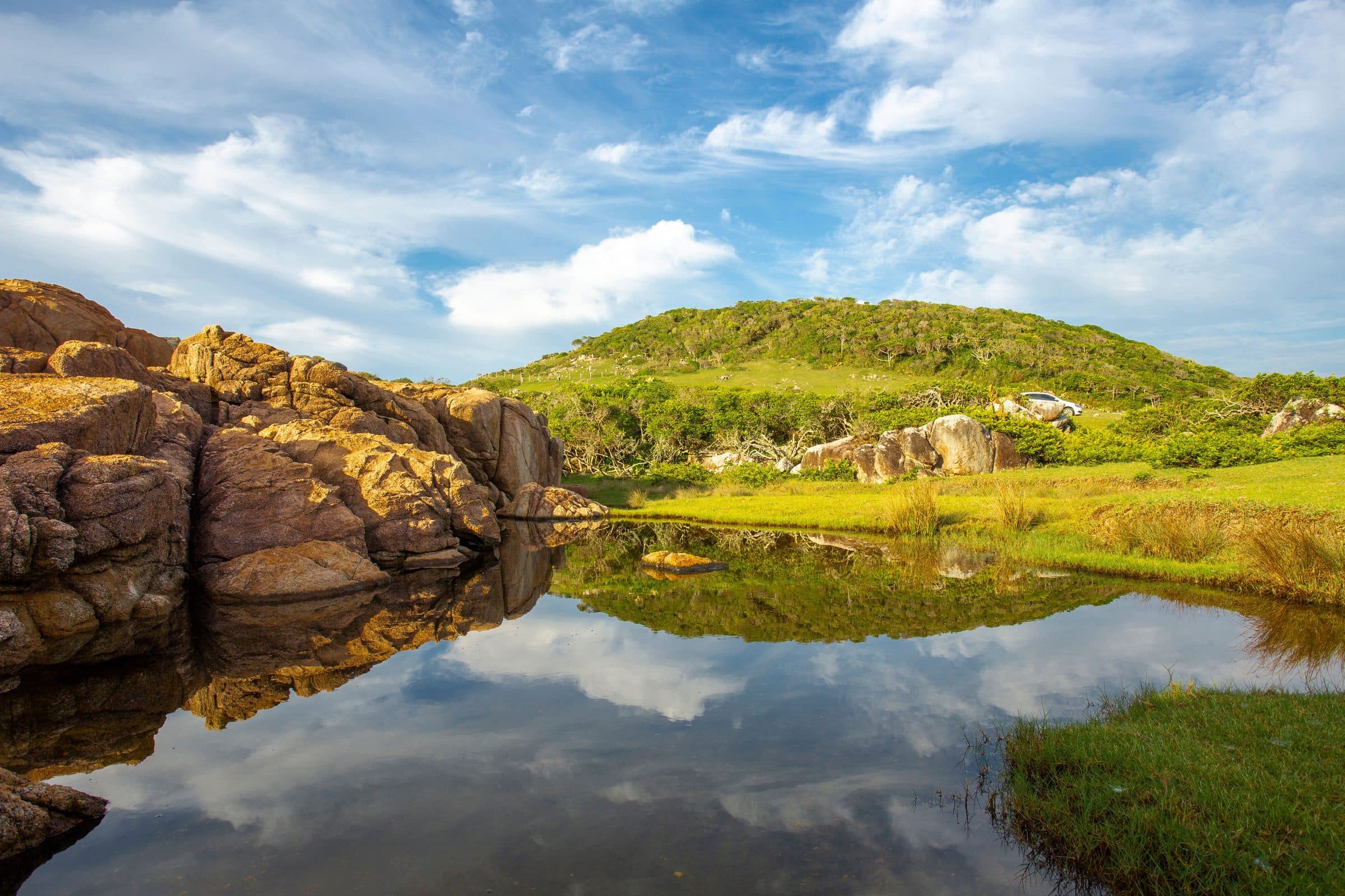 Paisagem rochosa com morro e reflexo na água clara em Ibiraquera