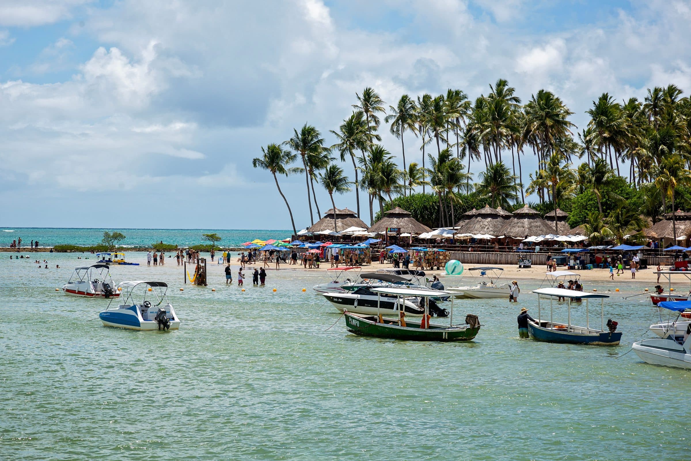 Praia tropical com pessoas na orla e barcos no mar