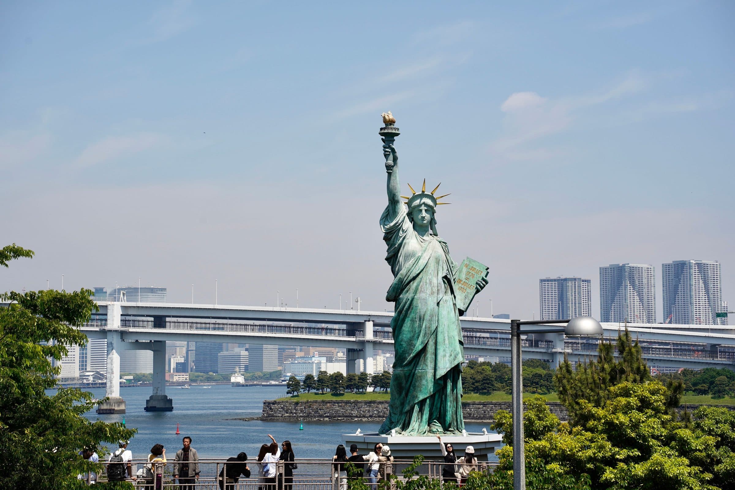 Réplica da Estátua da Liberdade na Baía de Tóquio com visitantes e prédios da cidade ao fundo