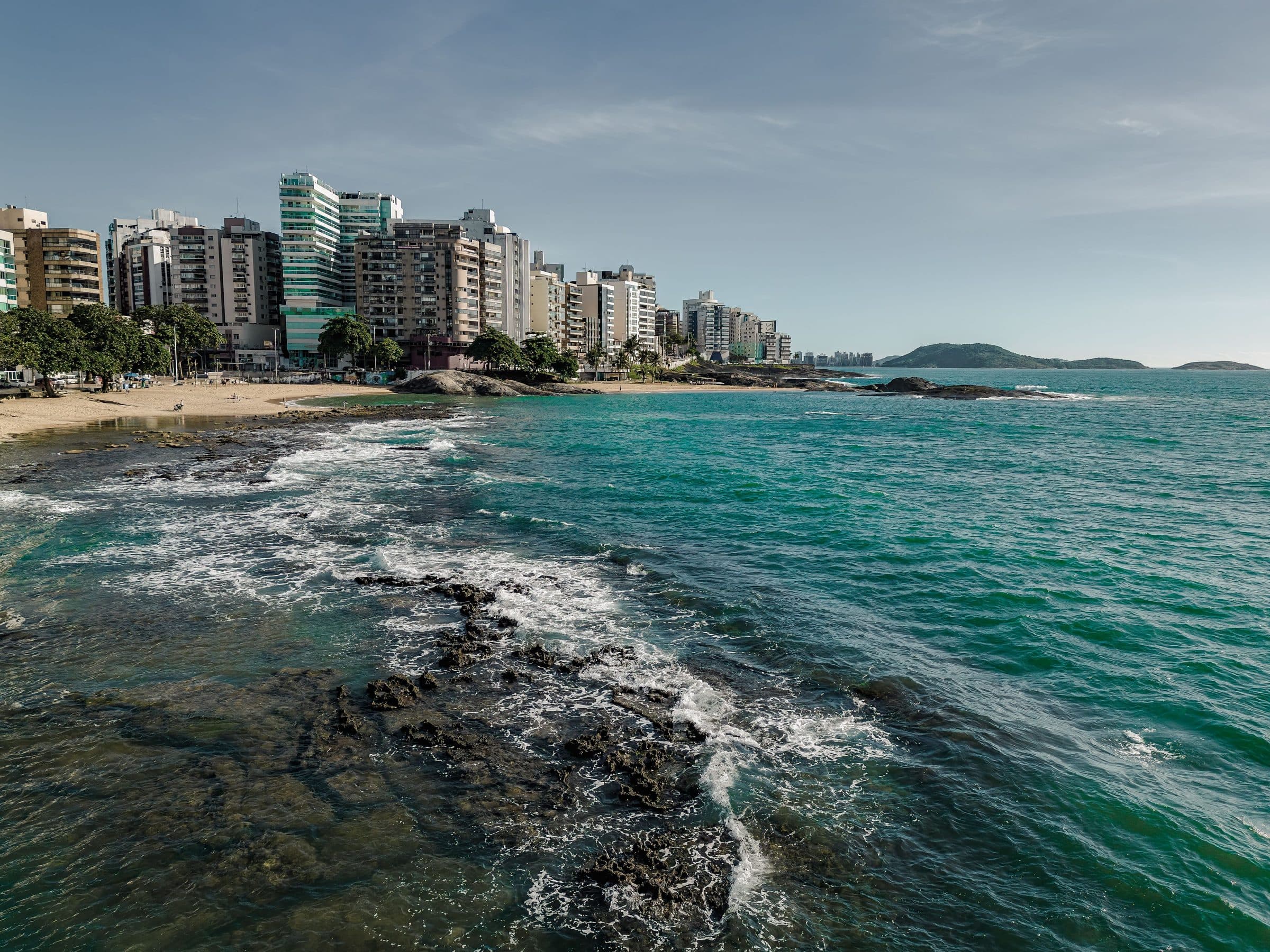 Vista da orla de Guarapari com prédios à beira-mar e águas azuis claras