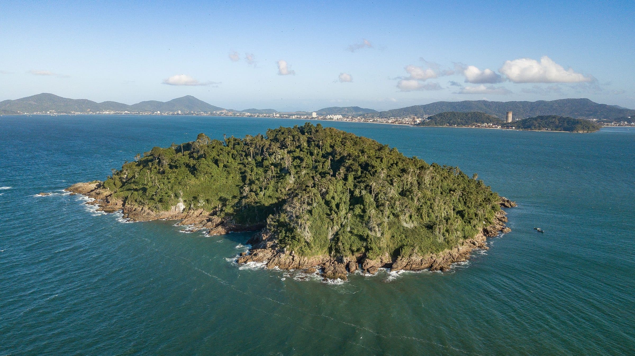 Vista aérea de uma ilha com vegetação cercada por águas azuis no litoral sul do Brasil