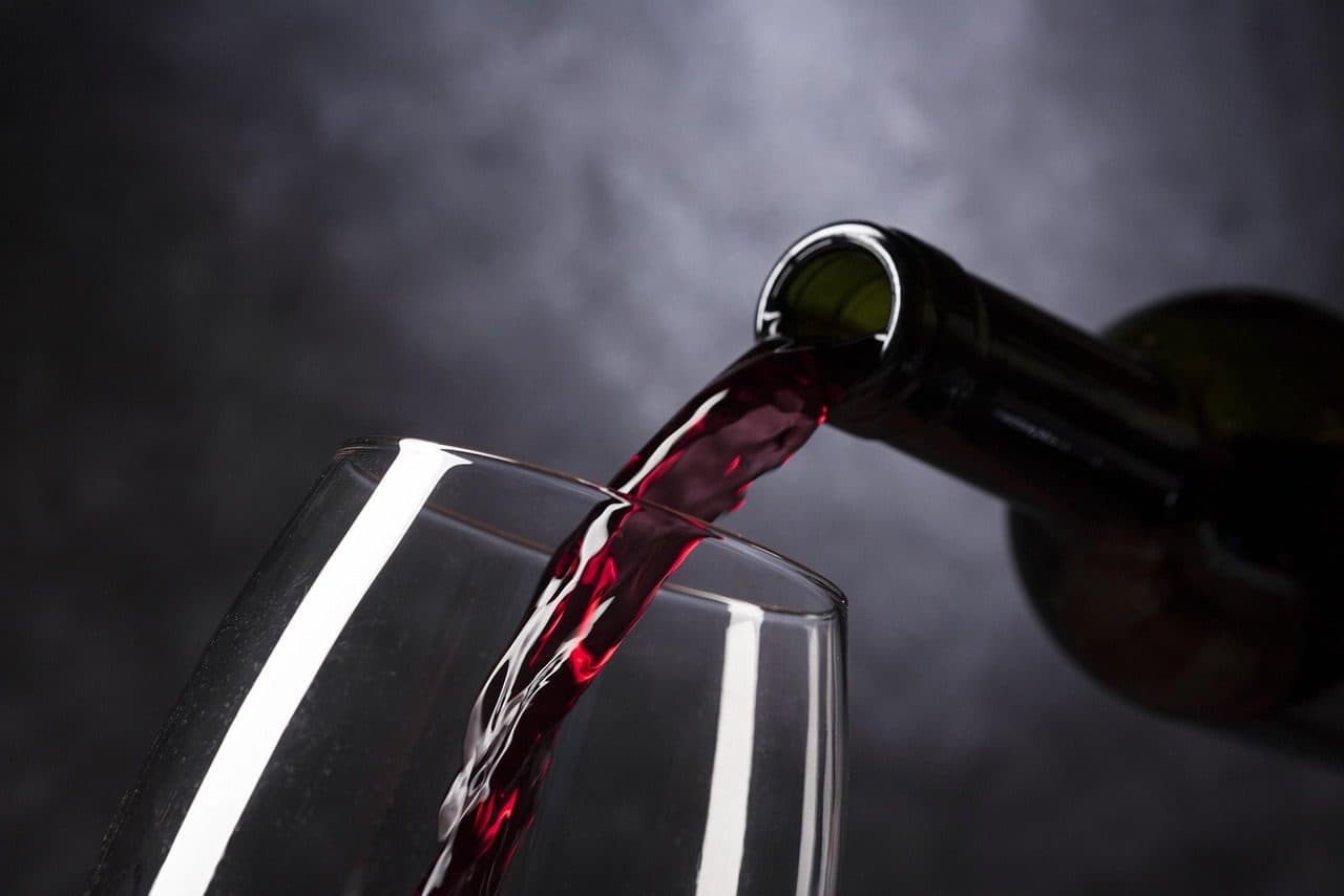Garrafa de vinho tinto ao lado de uma taça servida com vinho