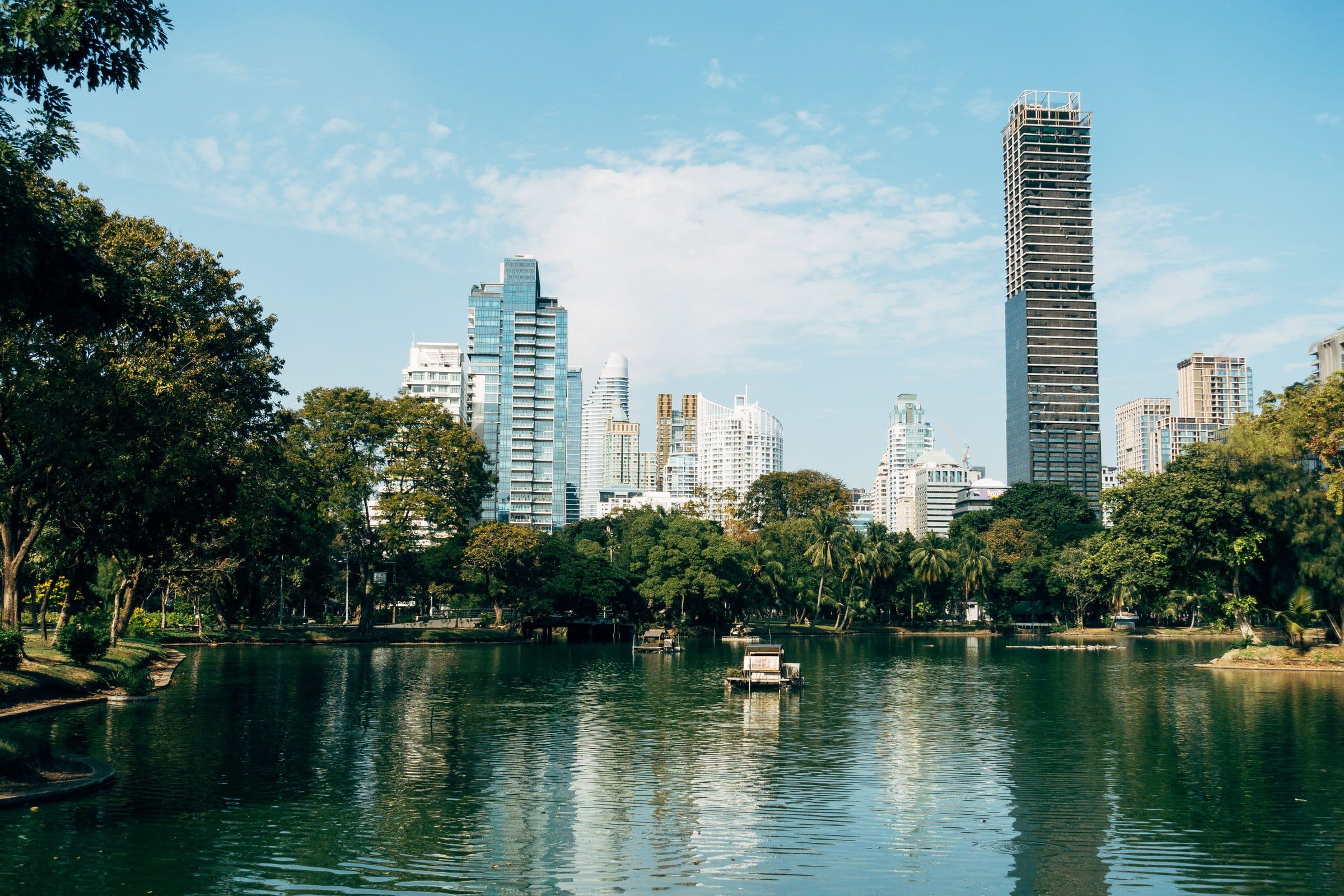 Vista dos arranha-céus de Bangkok refletidos no lago de um parque sob o céu azul