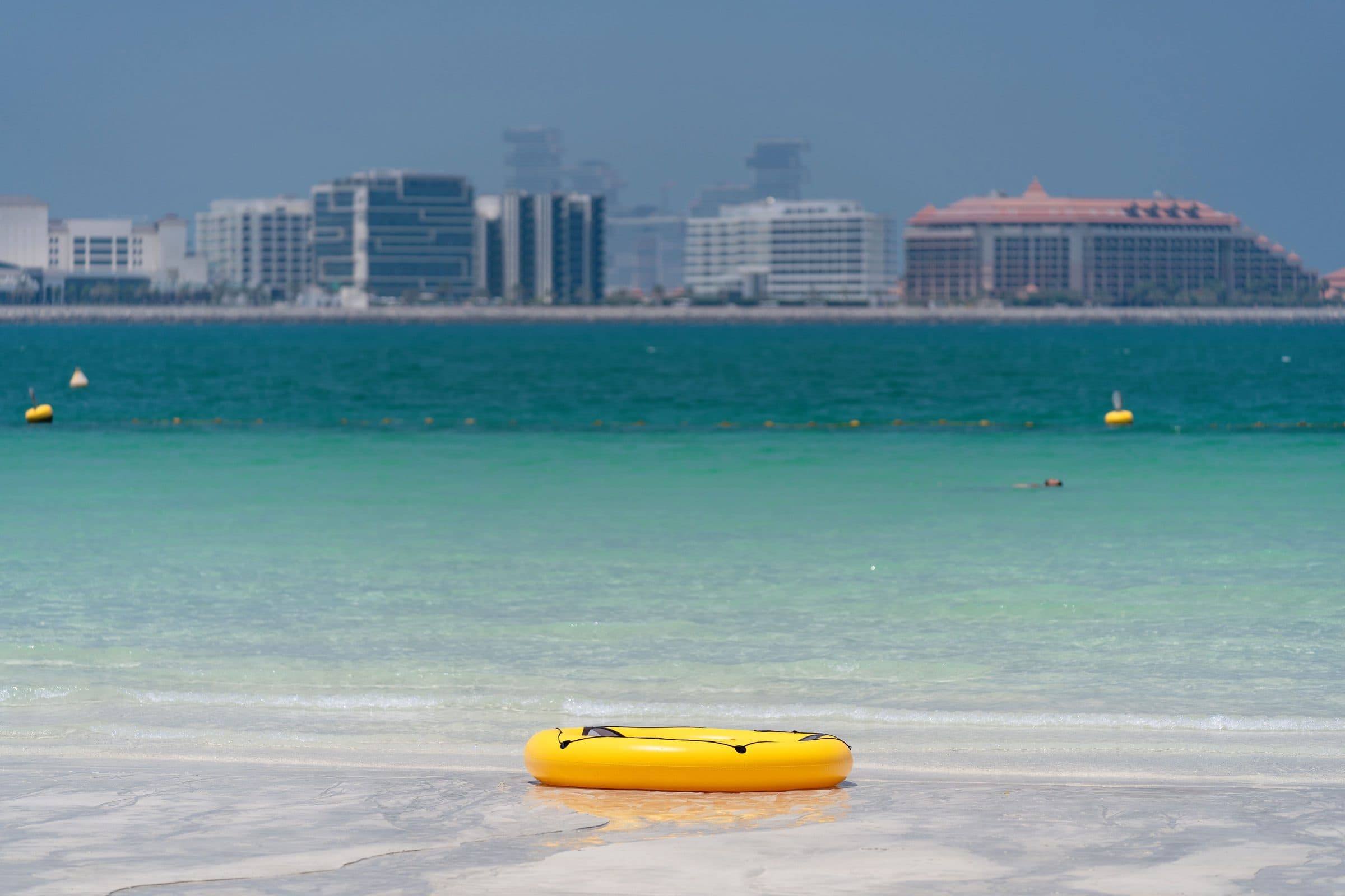 Boia inflável amarela na praia de Dubai com prédios da cidade ao fundo em dia claro