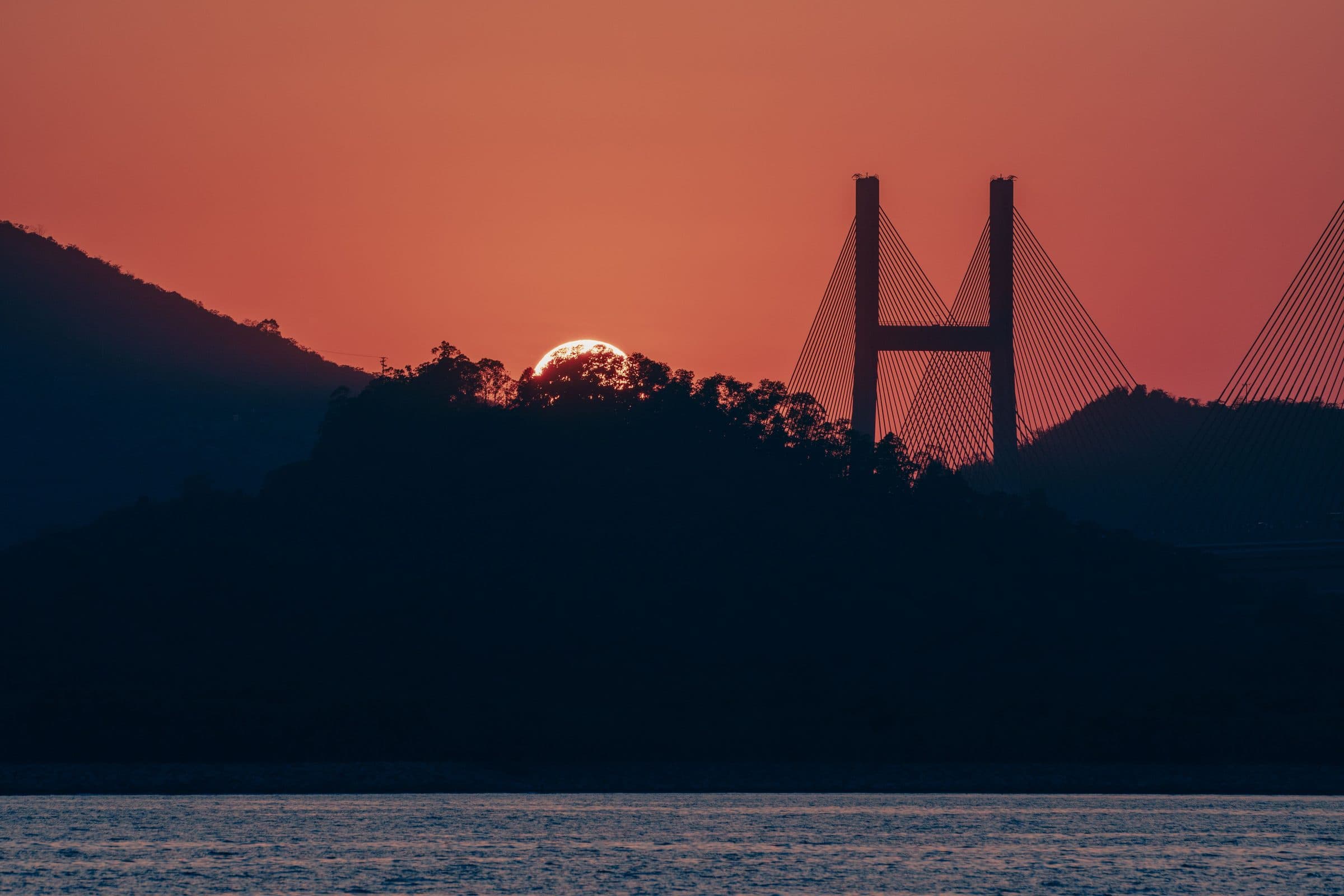 Pôr do sol com céu alaranjado sobre a Ponte Tsing Ma em Hong Kong