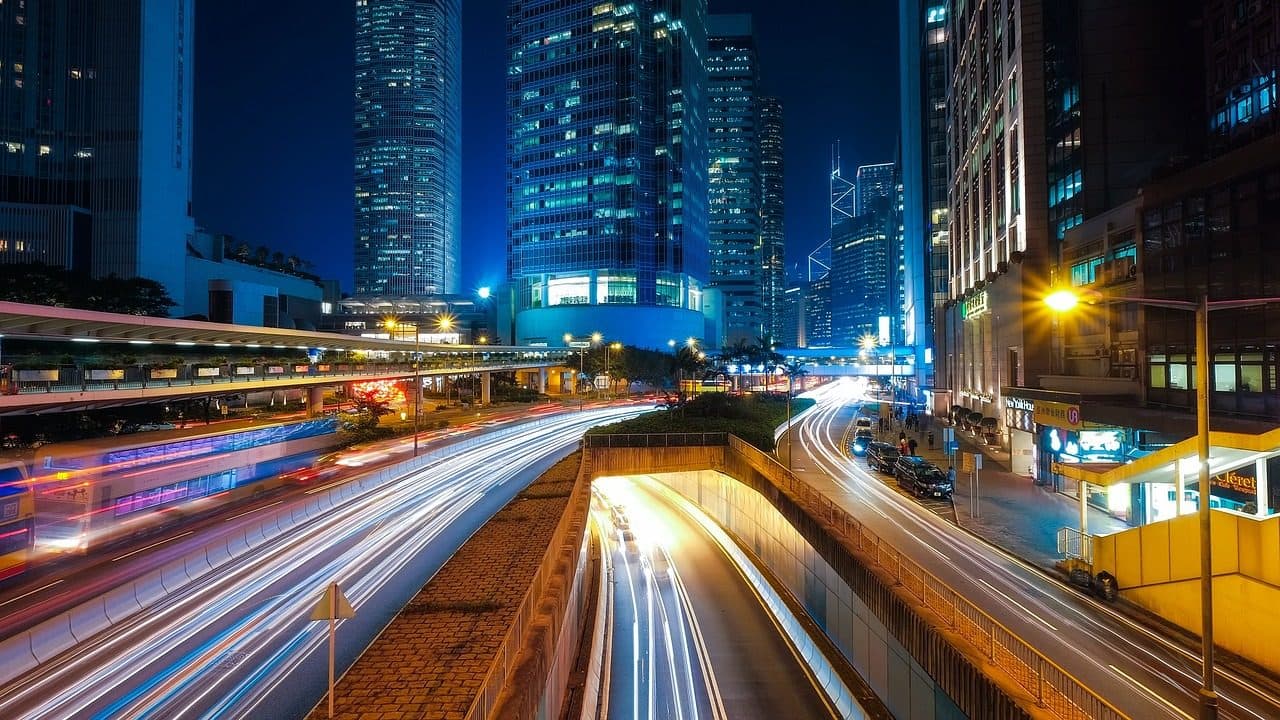 Trânsito noturno com rastros de luzes entre arranha-céus iluminados em Hong Kong