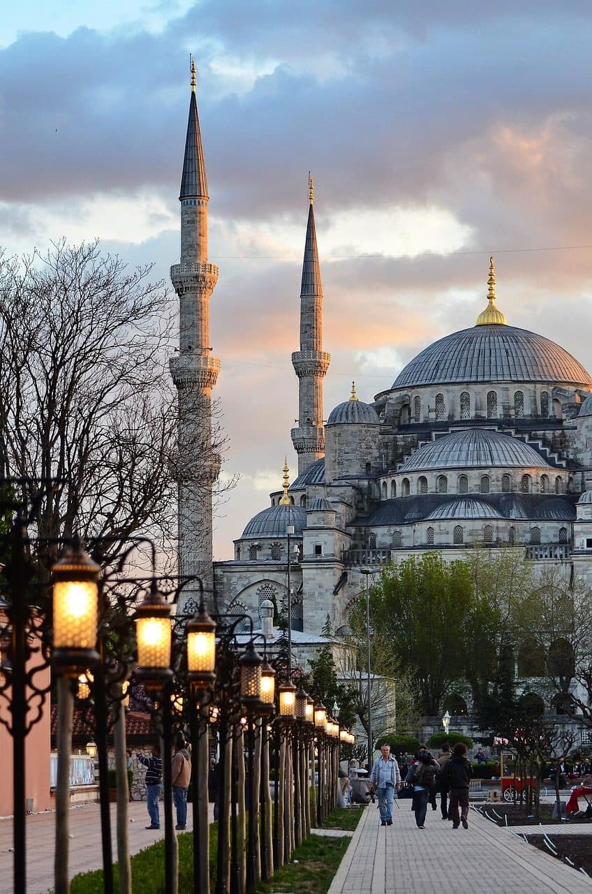 Rua de Istambul com postes de luz e vista para uma mesquita com minaretes ao pôr do sol.