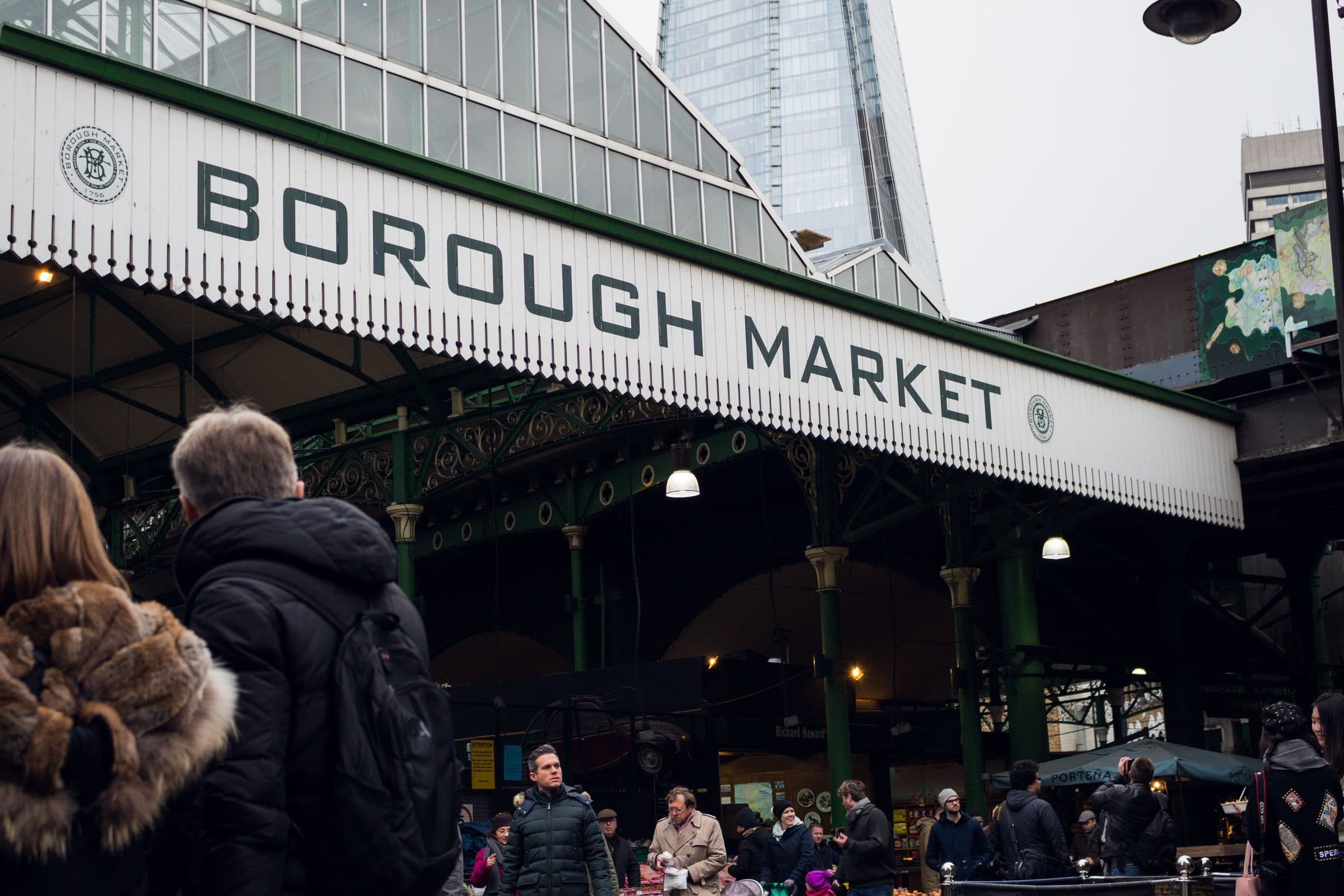 Pessoas caminham pelo Borough Market em Londres com arranha-céus ao fundo