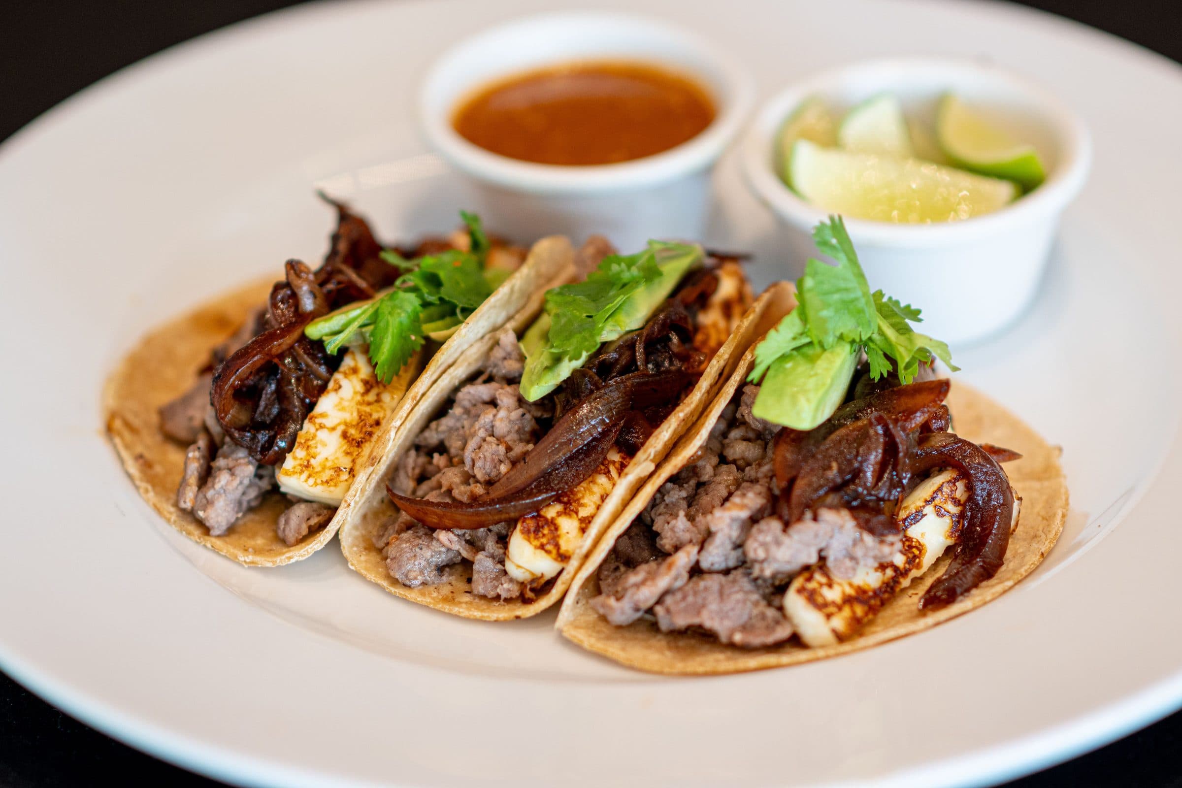 Tacos recheados com carne, queijo, cebola e coentro, servidos com limão e molho