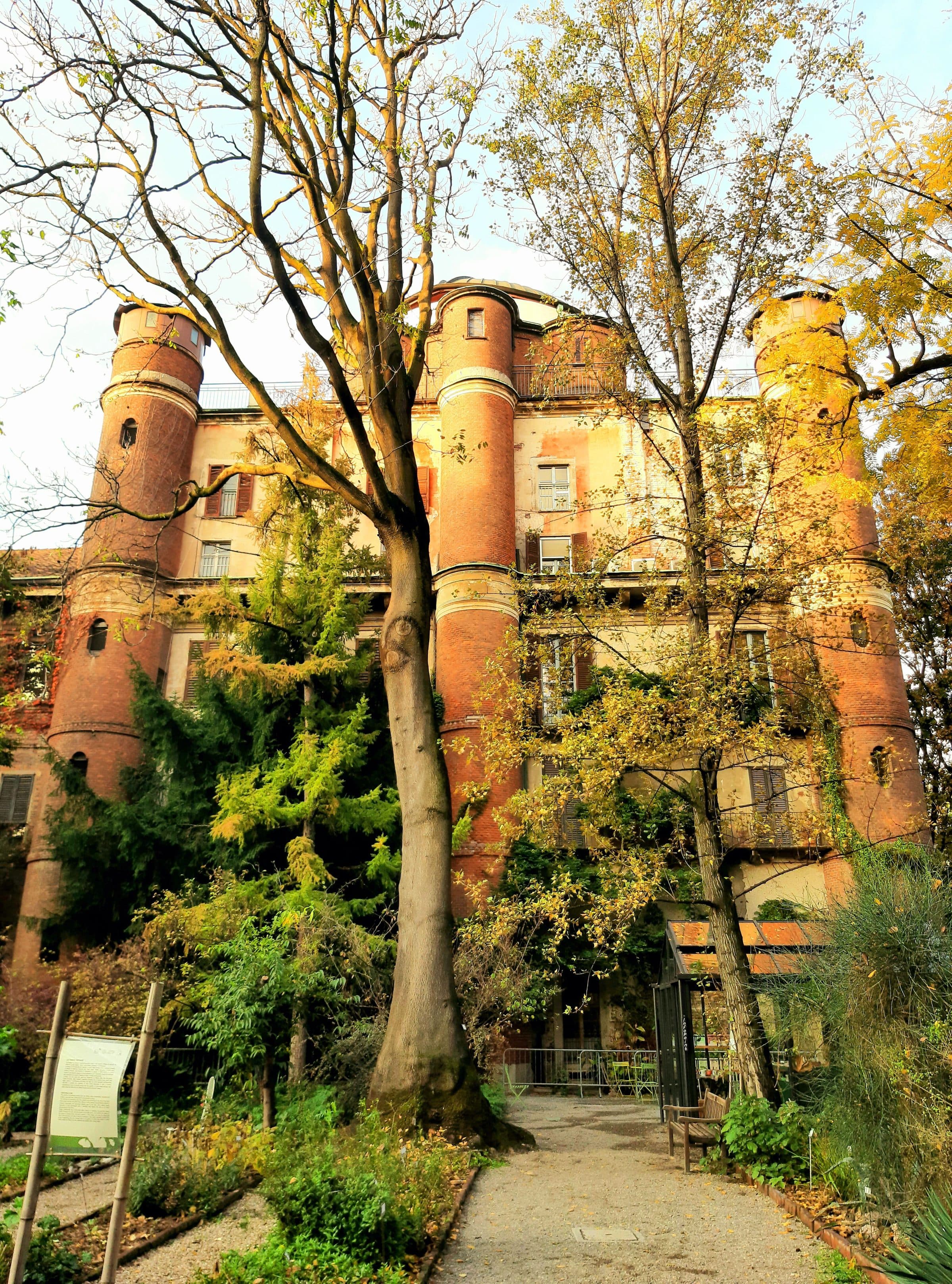 Edifício histórico de tijolos vermelhos cercado por árvores com folhas de outono em Milão