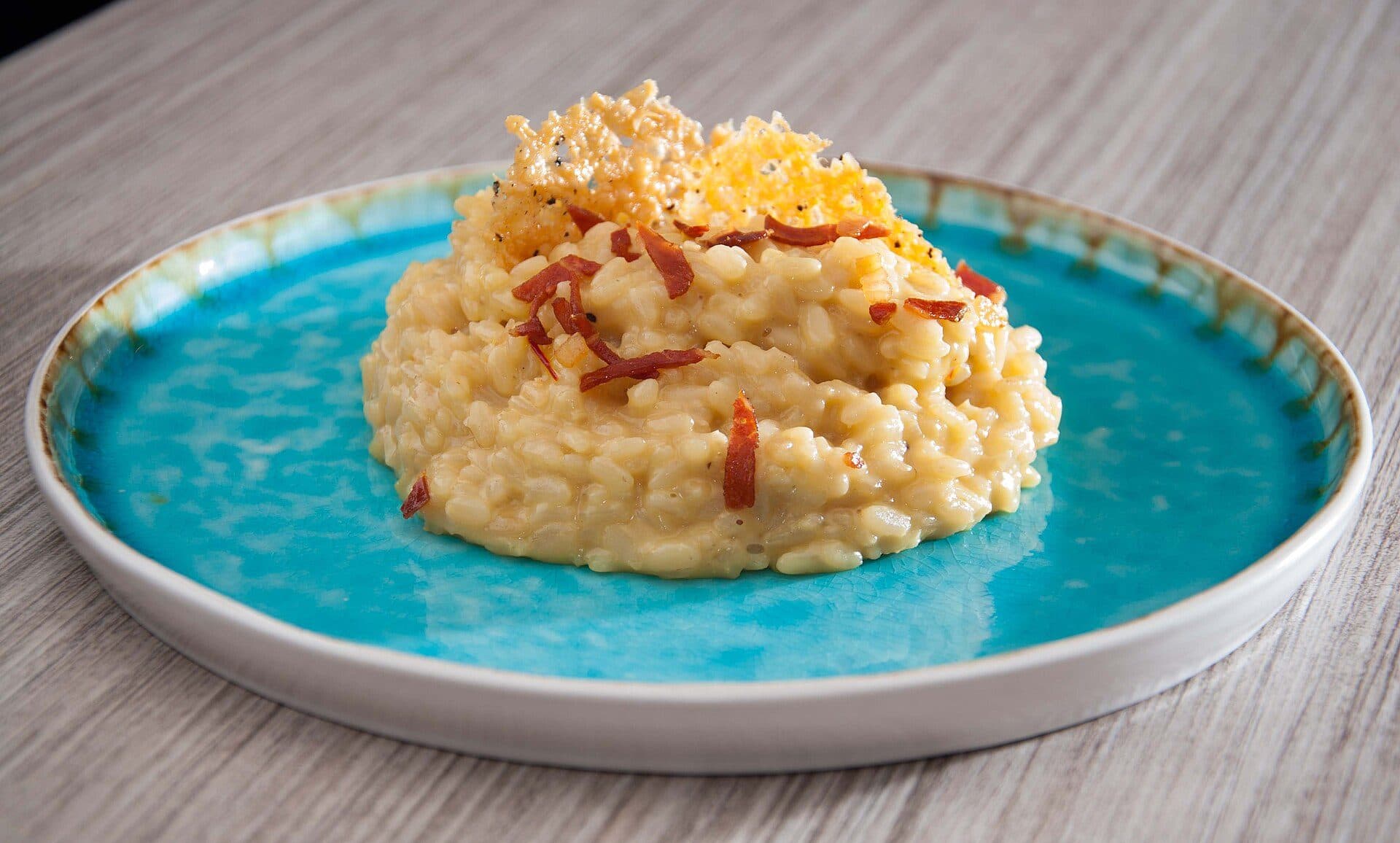 Prato de risotto alla milanese servido com biscoito de parmesão e presunto italiano grelhado