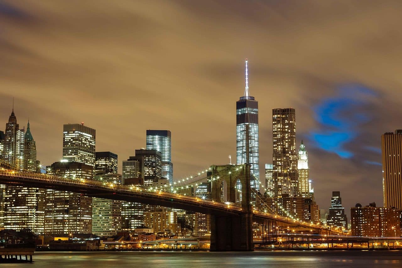Vista noturna da Brooklyn Bridge iluminada sobre o rio com os arranha-céus de Nova York ao fundo