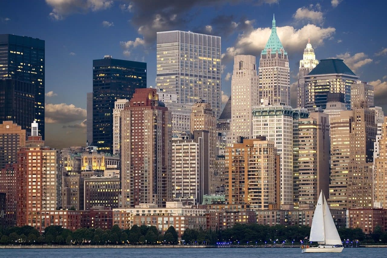 Skyline de Manhattan com arranha-céus e veleiro no rio Hudson ao entardecer