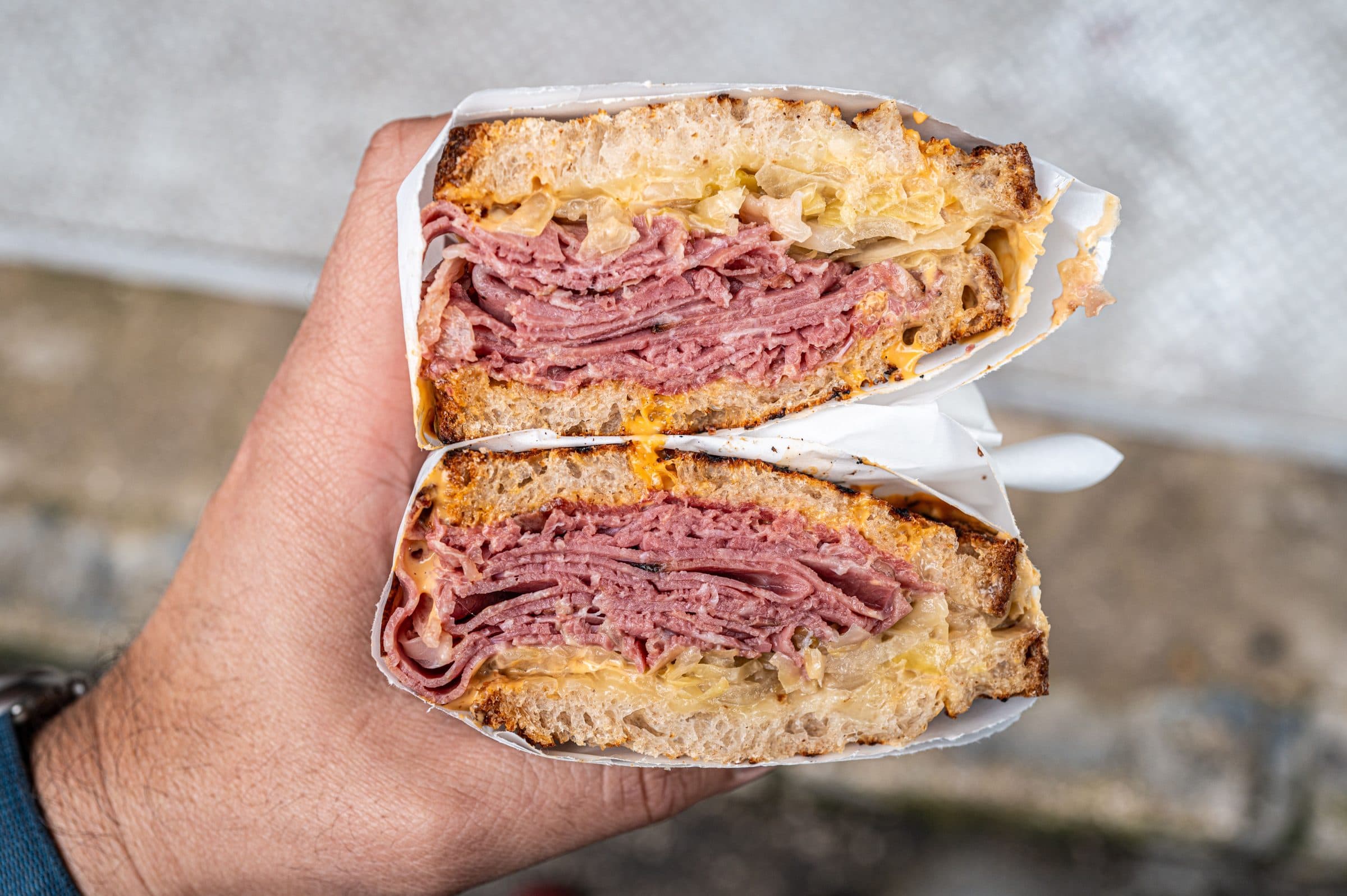 Pessoa segurando um sanduíche de pastrami em primeiro plano