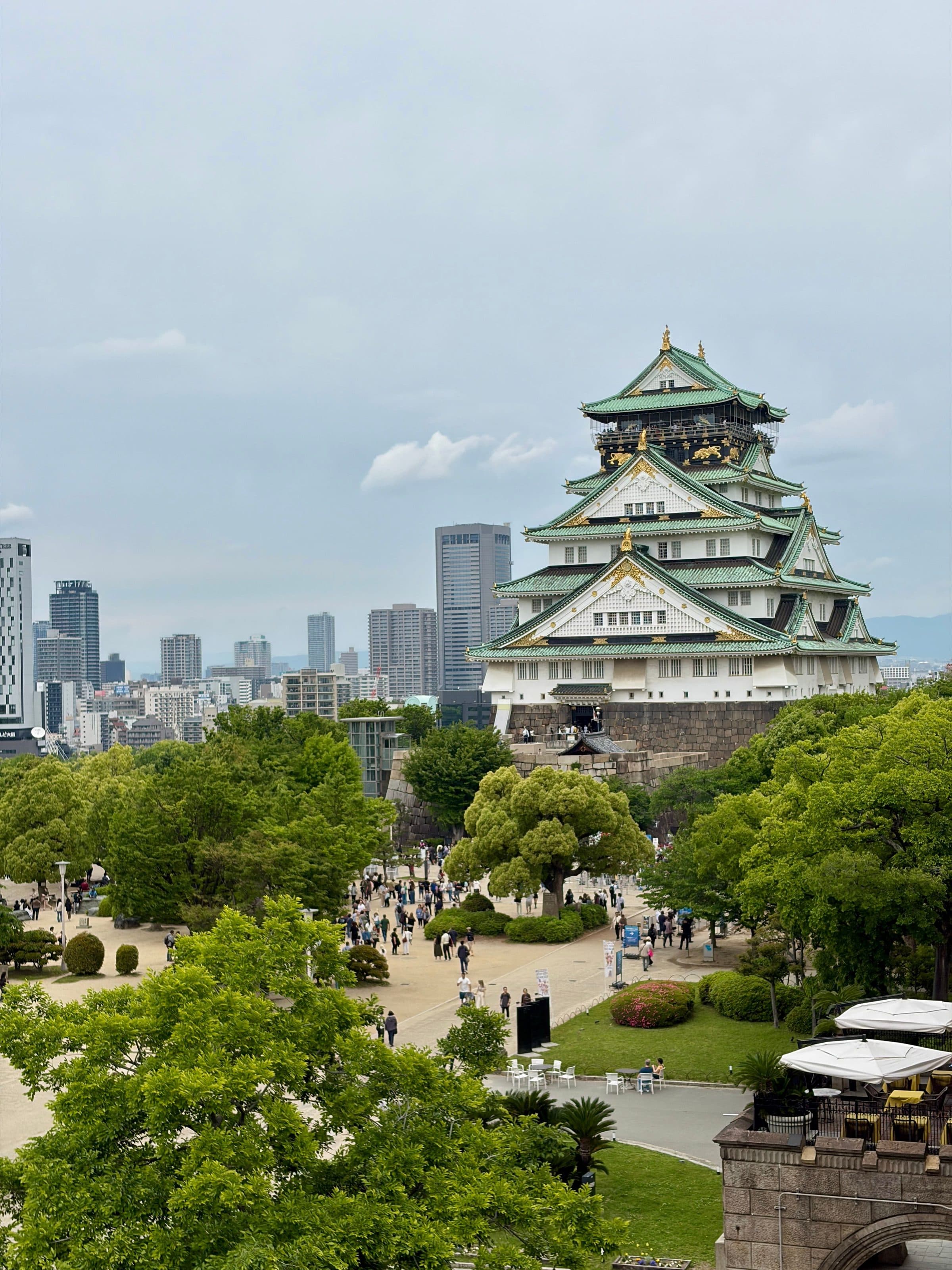Vista do Castelo de Osaka cercado por área verde e prédios sob céu nublado