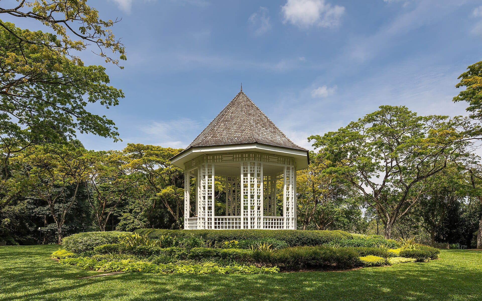 Coreto e árvores verdes em tarde ensolarada com céu azul no Singapore Botanic Gardens