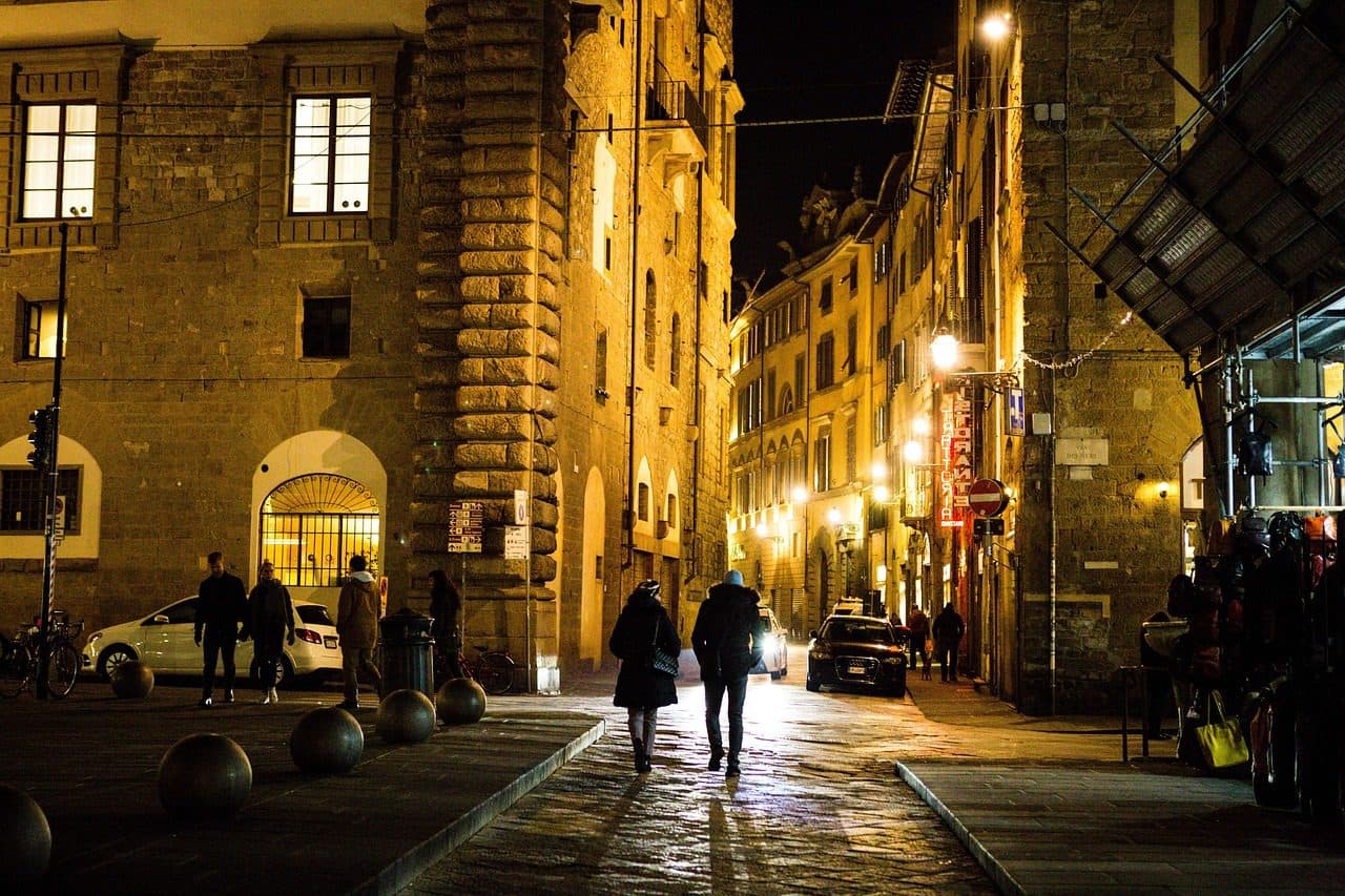 Rua histórica de Florença à noite com pessoas caminhando entre edifícios antigos