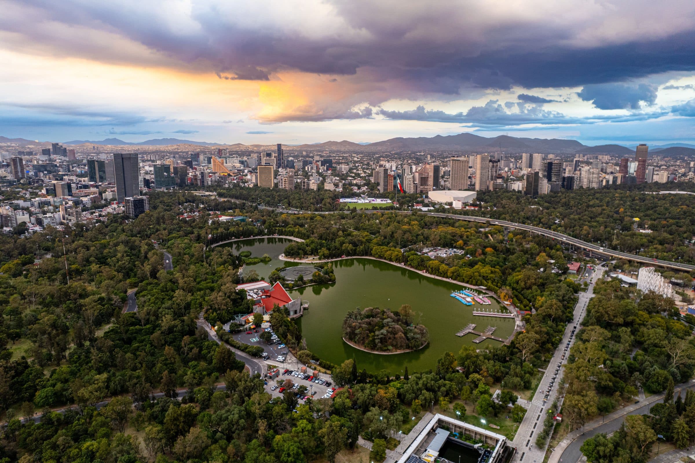 Vista aérea do Parque Chapultepec na Cidade do México ao pôr do sol, com vegetação e o horizonte urbano