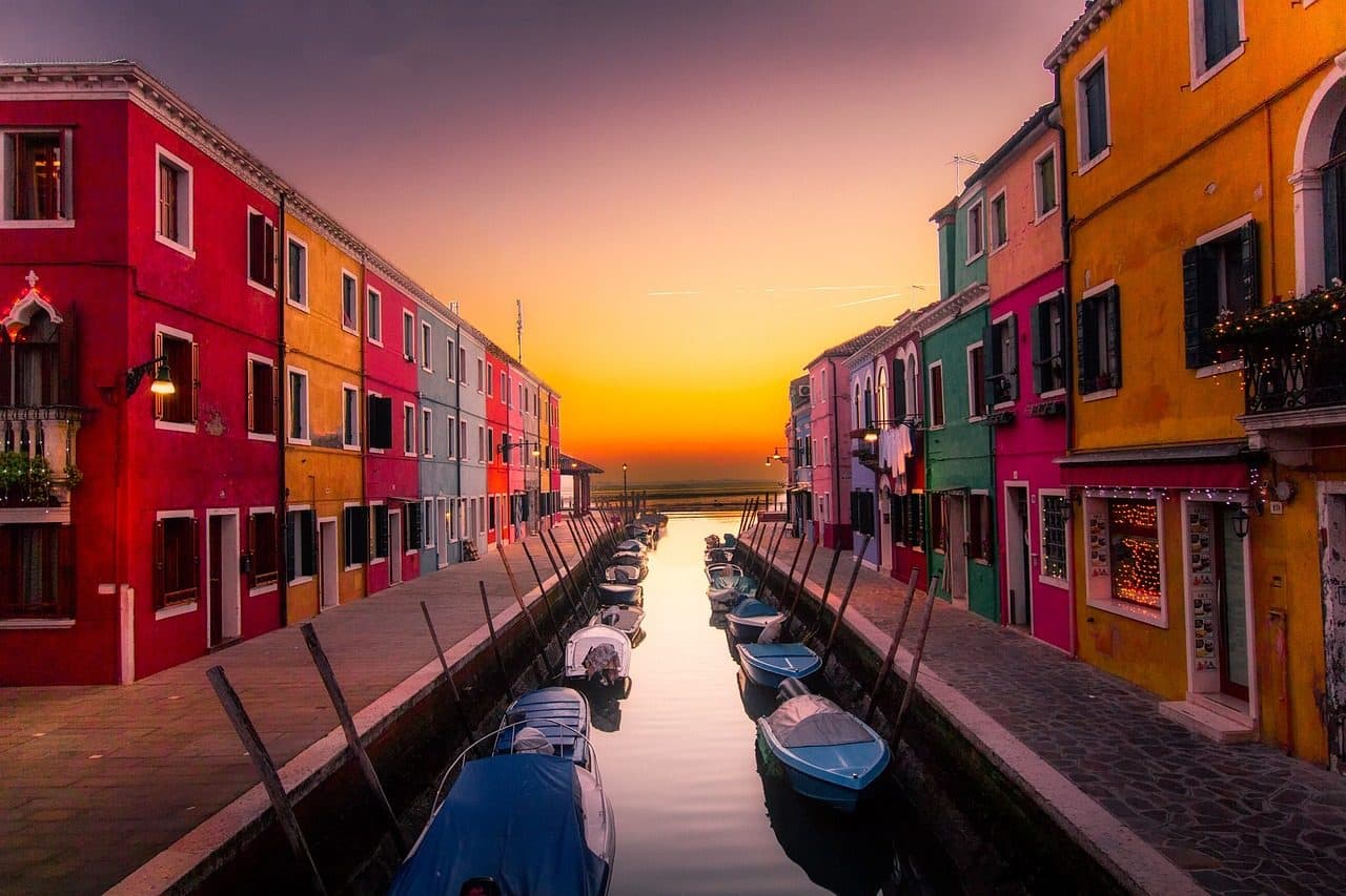 Casas coloridas e barcos ancorados em canal na Ilha de Burano durante o entardecer