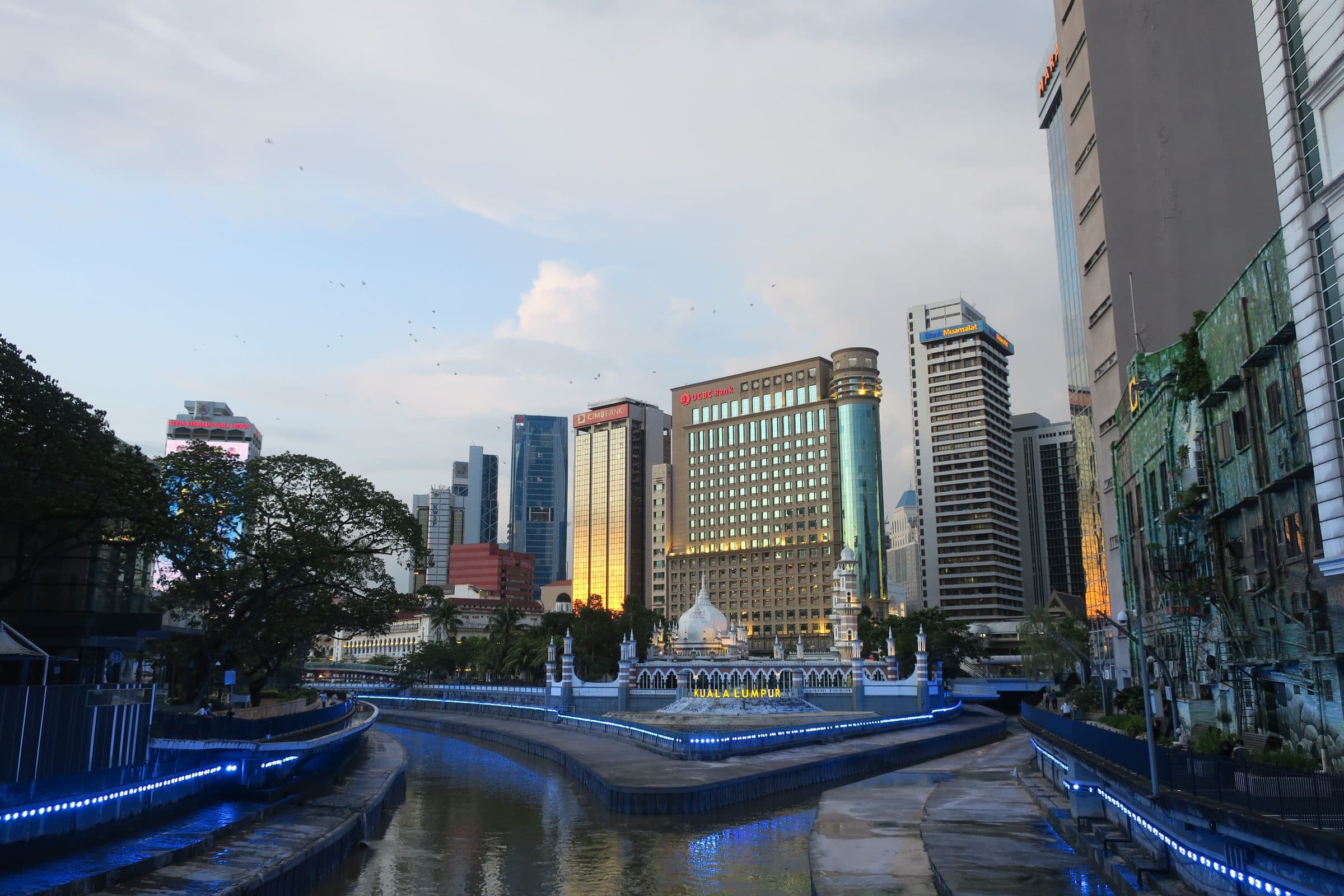 Horizonte de Kuala Lumpur ao pôr do sol com edifícios modernos e um rio em primeiro plano