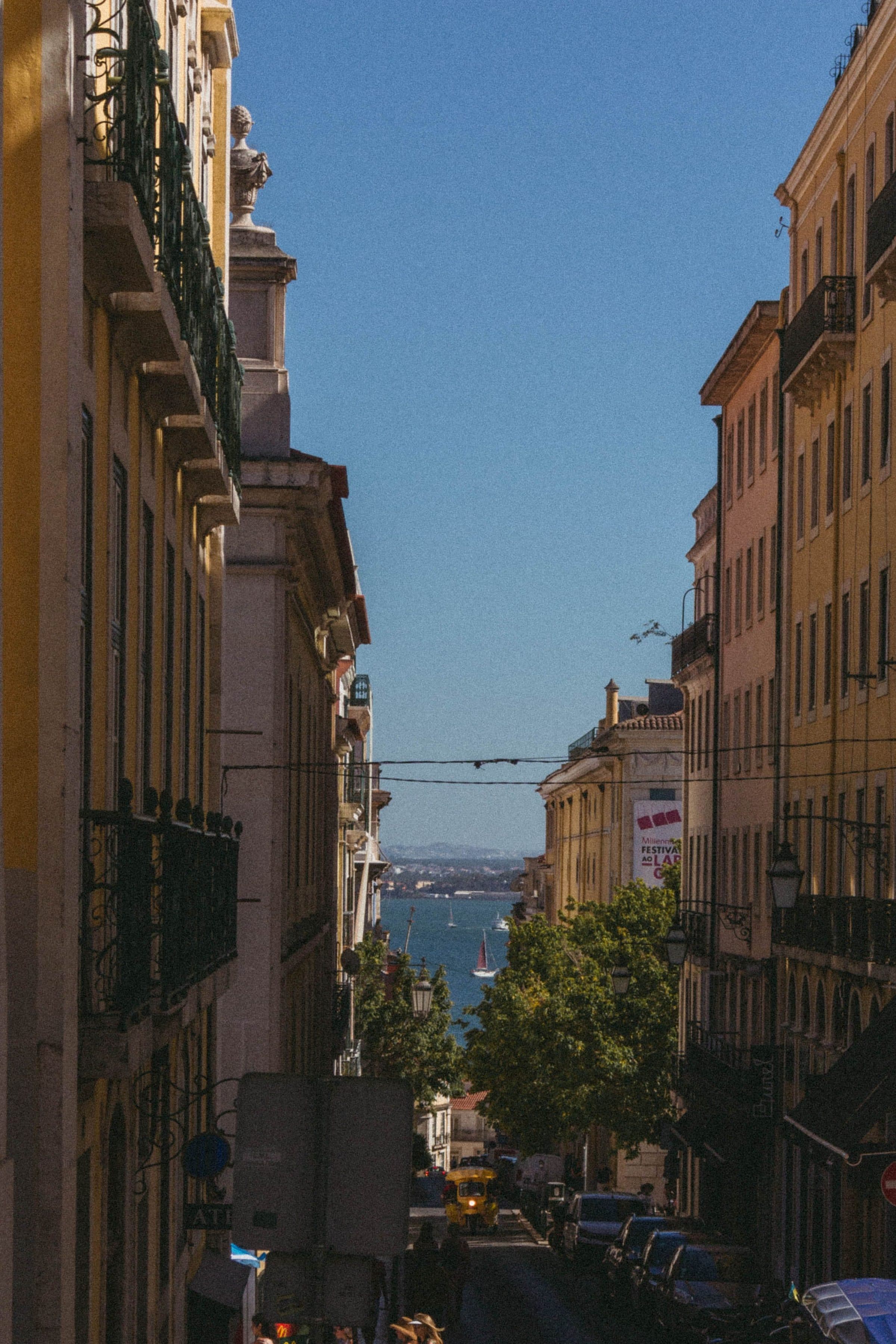 Rua estreita em Lisboa com arquitetura clássica e vista para o mar sob céu azul