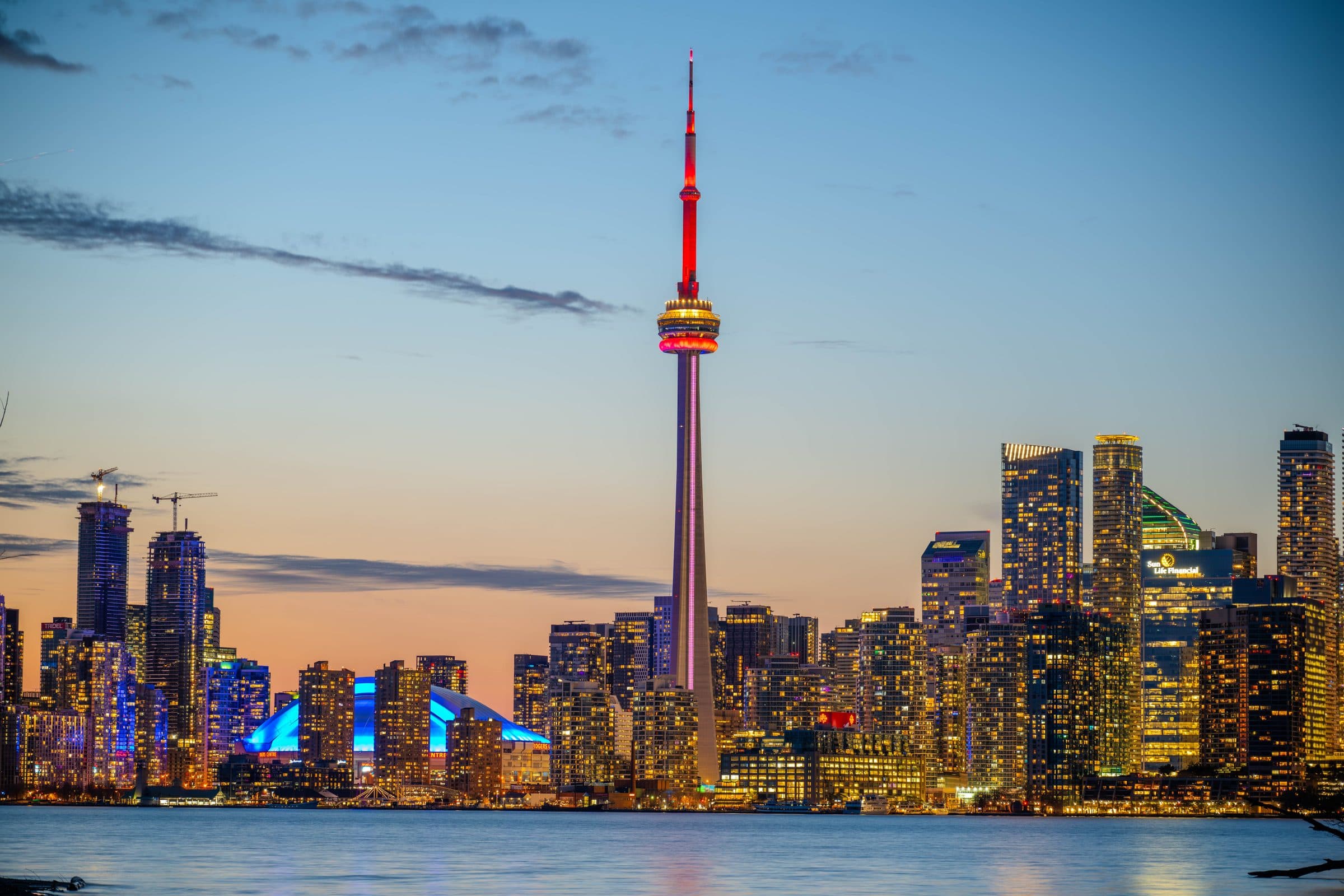 Linha do horizonte de Toronto ao pôr do sol com a CN Tower e luzes da cidade refletidas no lago
