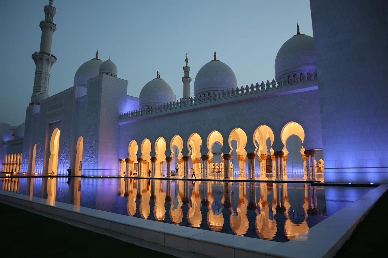 Fachada da Mesquita Sheikh Zayed em Abu Dhabi com cúpulas de mármore branco e reflexo na água