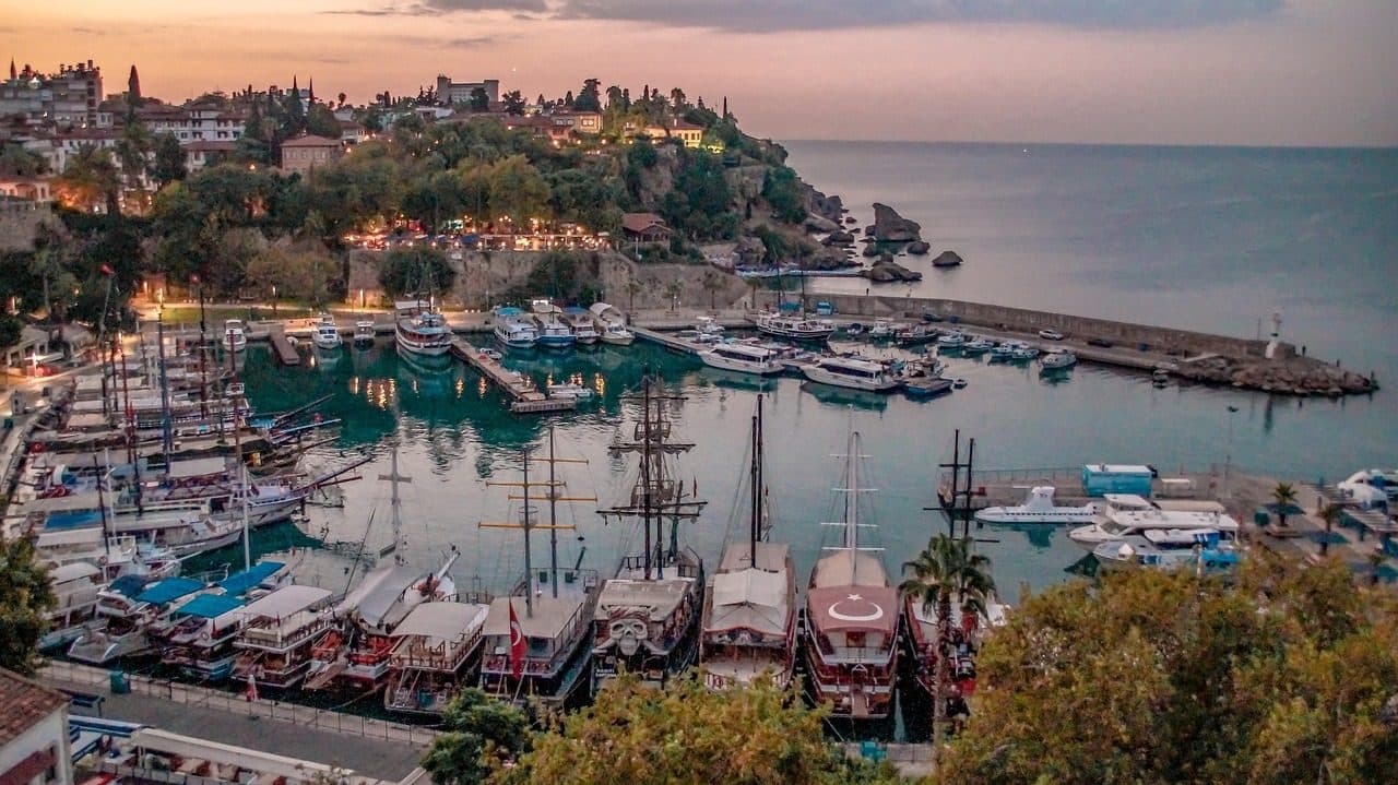 Amanhecer no porto de Antalya com barcos atracados no mar e a cidade ao fundo