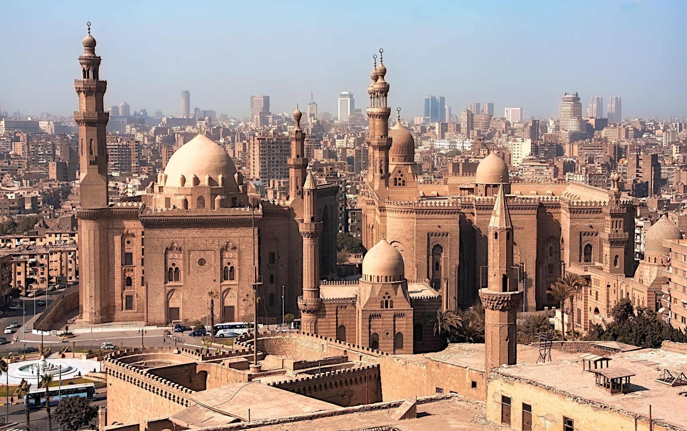 Vista aérea de mesquitas históricas com arquitetura islâmica e a cidade do Cairo ao fundo