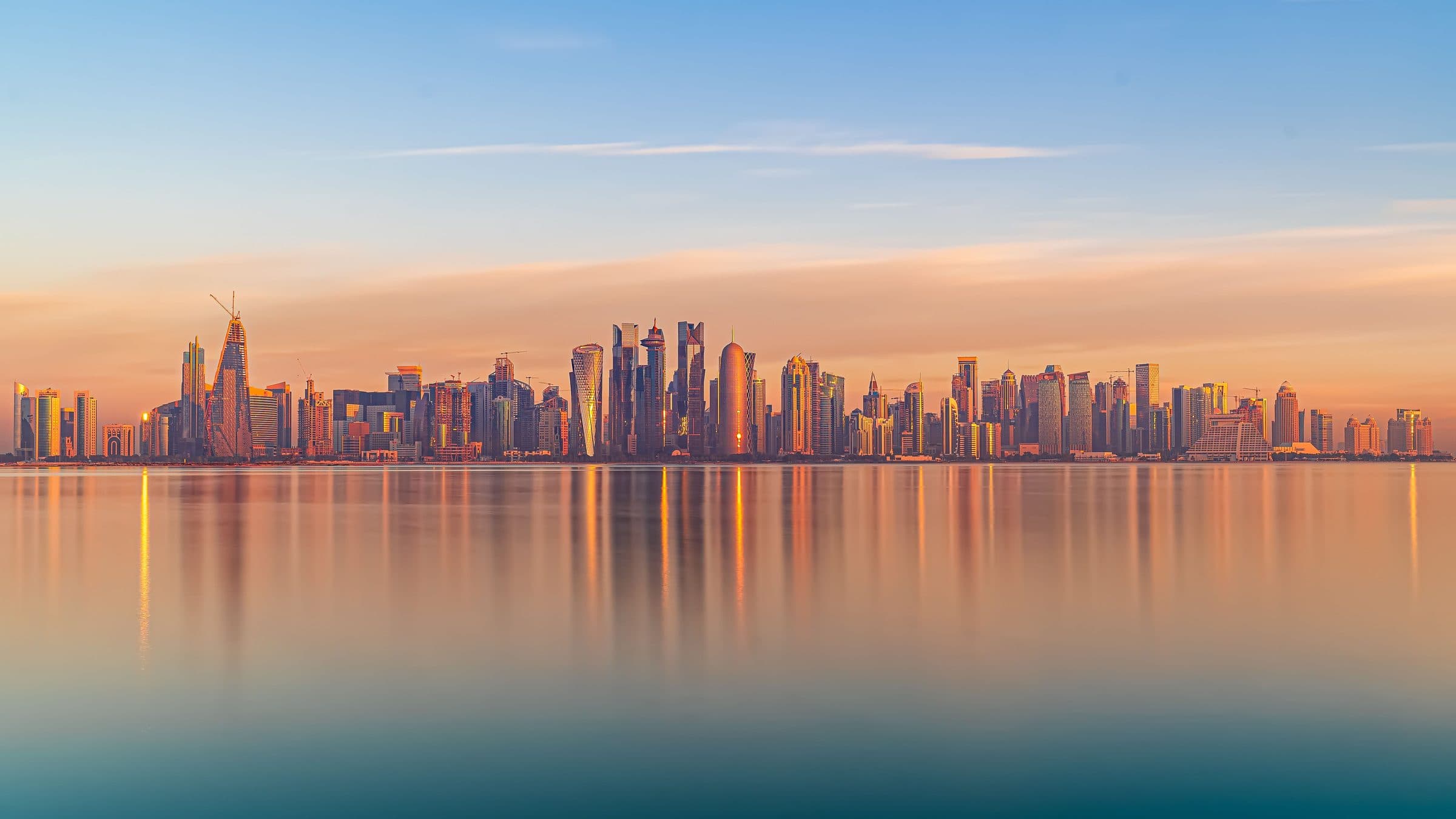 Arranha-céus modernos refletidos no mar calmo durante o pôr do sol em Doha
